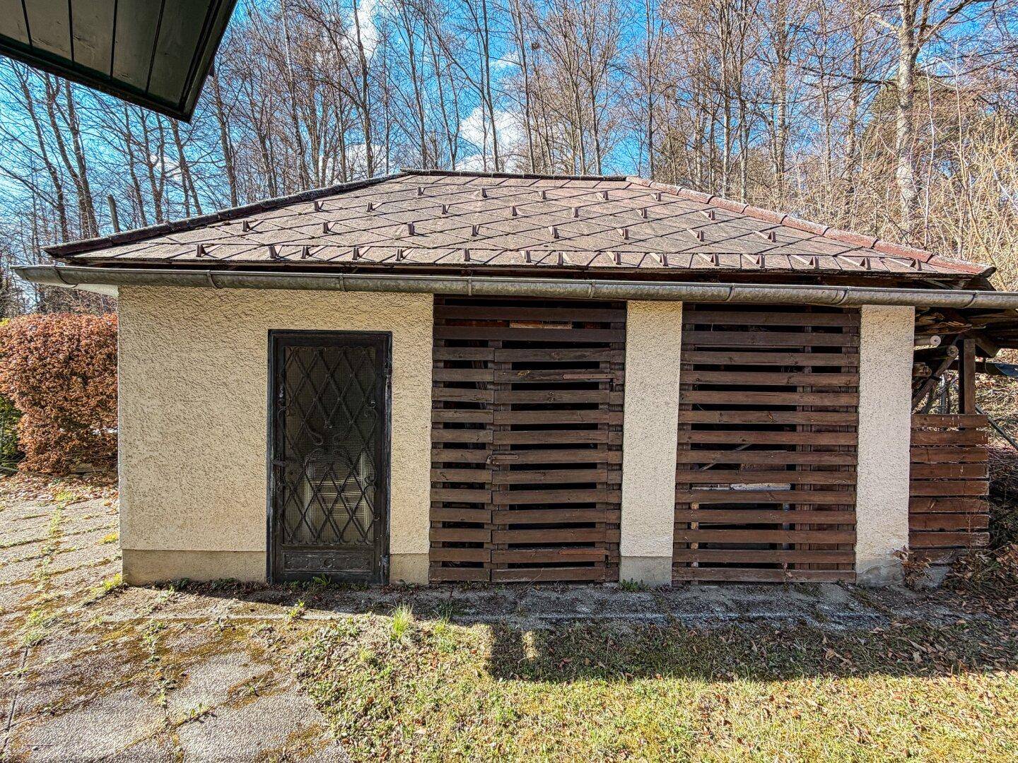 Kleines Nebengebäude mit Ziegeldach und Holzverkleidung, möglicherweise ein Geräteschuppen im Garten.