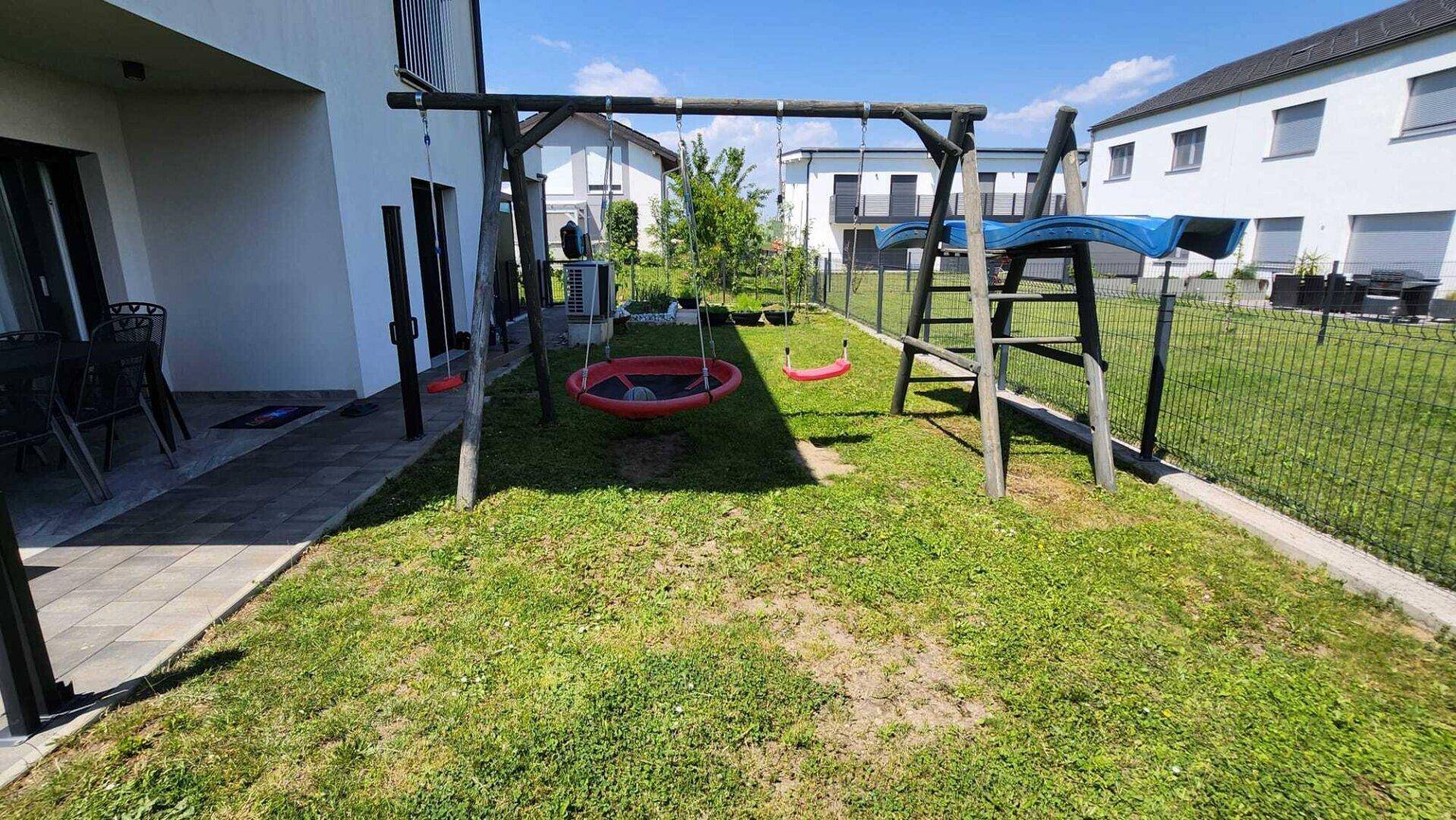 Gepflegter Gartenbereich mit Kinderschaukel und einer kleinen gepflasterten Terrasse für Outdoor-Aktivitäten.