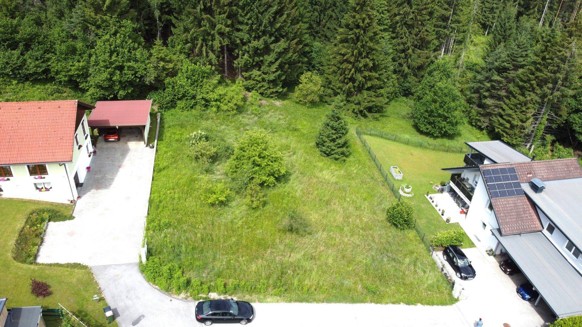 Drohnenaufnahme eines Grundstücks mit Wohnhaus, Carport und umgebendem Waldgebiet.