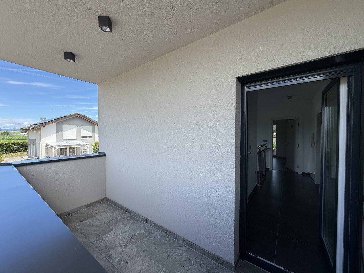 Heller Balkon mit Fliesenboden und Blick auf die umliegende Wohngegend und die Landschaft.