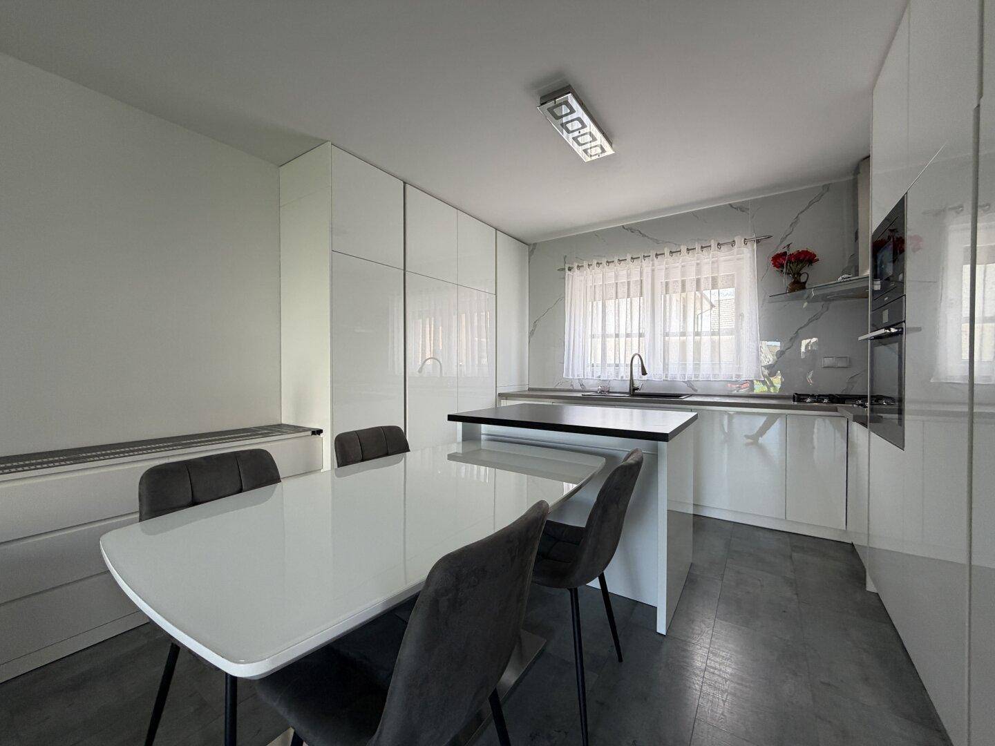Moderne weiße Küche mit Hochglanzfronten, Kücheninsel und integriertem Essbereich für die Familie.
