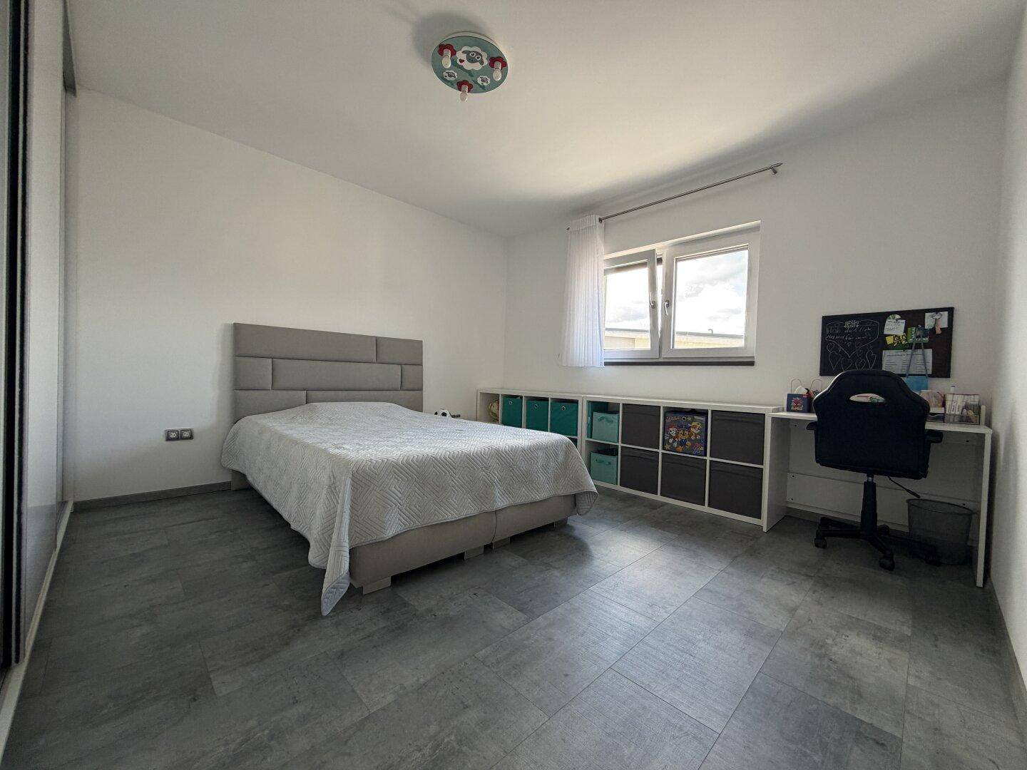 Helles Kinderzimmer mit Bett, Schreibtisch und praktischen Aufbewahrungslösungen unter dem Fenster.