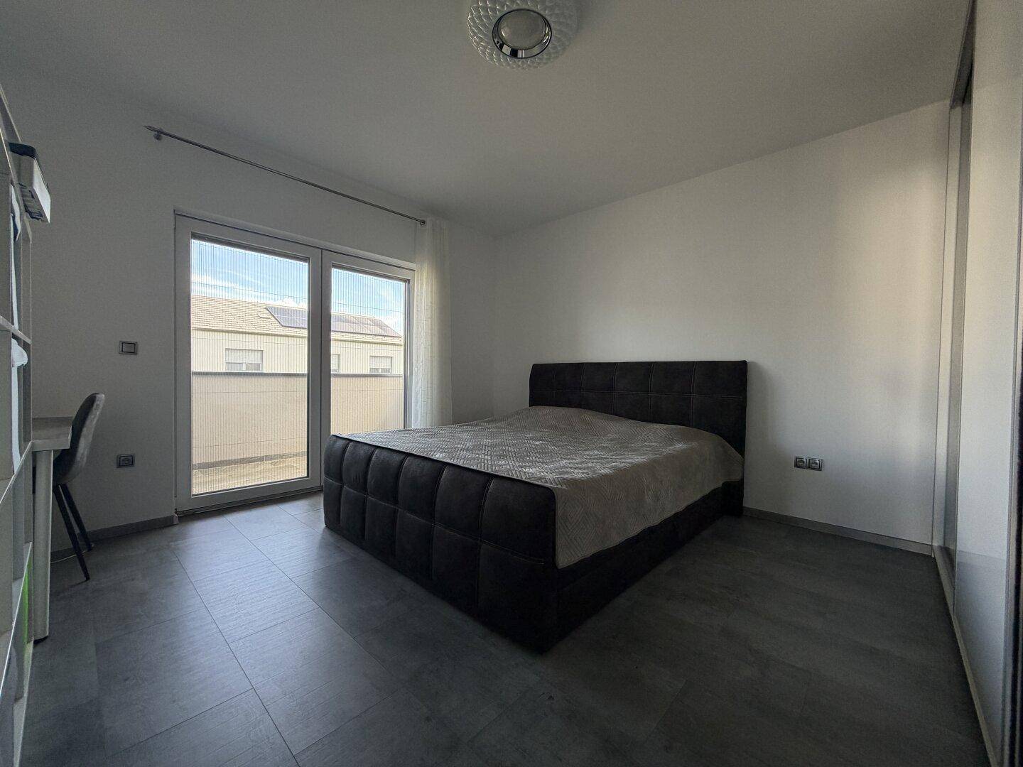 Geräumiges Schlafzimmer mit Doppelbett und großer Schiebetür, die auf einen sonnigen Balkon führt.
