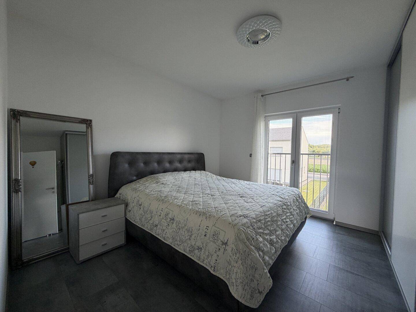 Gemütliches Schlafzimmer mit Doppelbett, großem Spiegel und direktem Zugang zu einem französischen Balkon.
