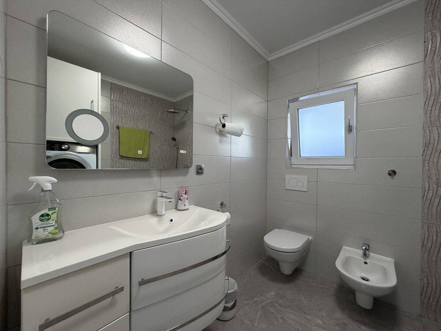 Modernes Badezimmer mit Dusche, WC, Bidet und einem stilvollen Waschtisch mit integriertem Spiegel.