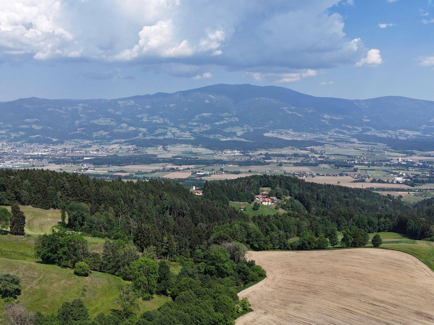 Weitläufige Landschaftsaufnahme mit Wäldern, Feldern und Bergen unter einem bewölkten Himmel.