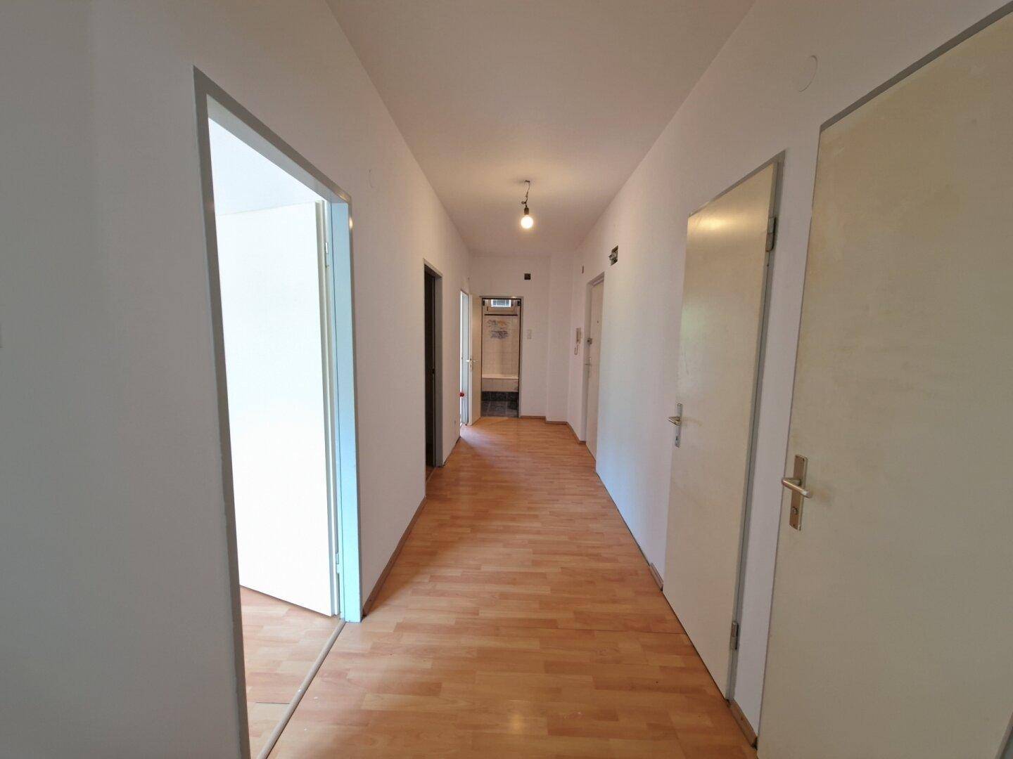 Langer, heller Flur mit hellem Laminatboden und weißen Wänden, der zu weiteren Räumen führt.