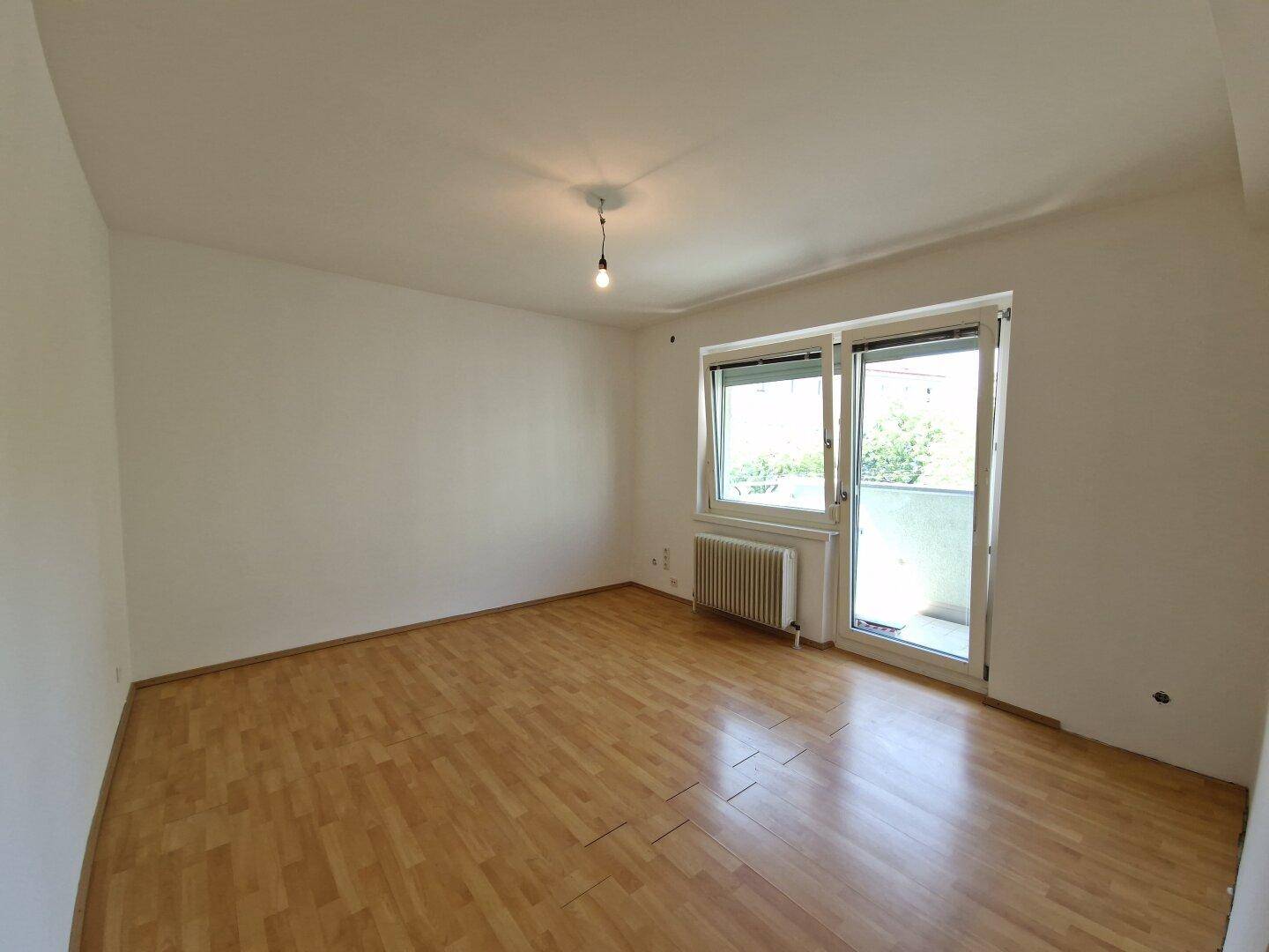 Heller Wohnraum mit Laminatboden und Zugang zu einem Balkon, ideal für entspannte Stunden.