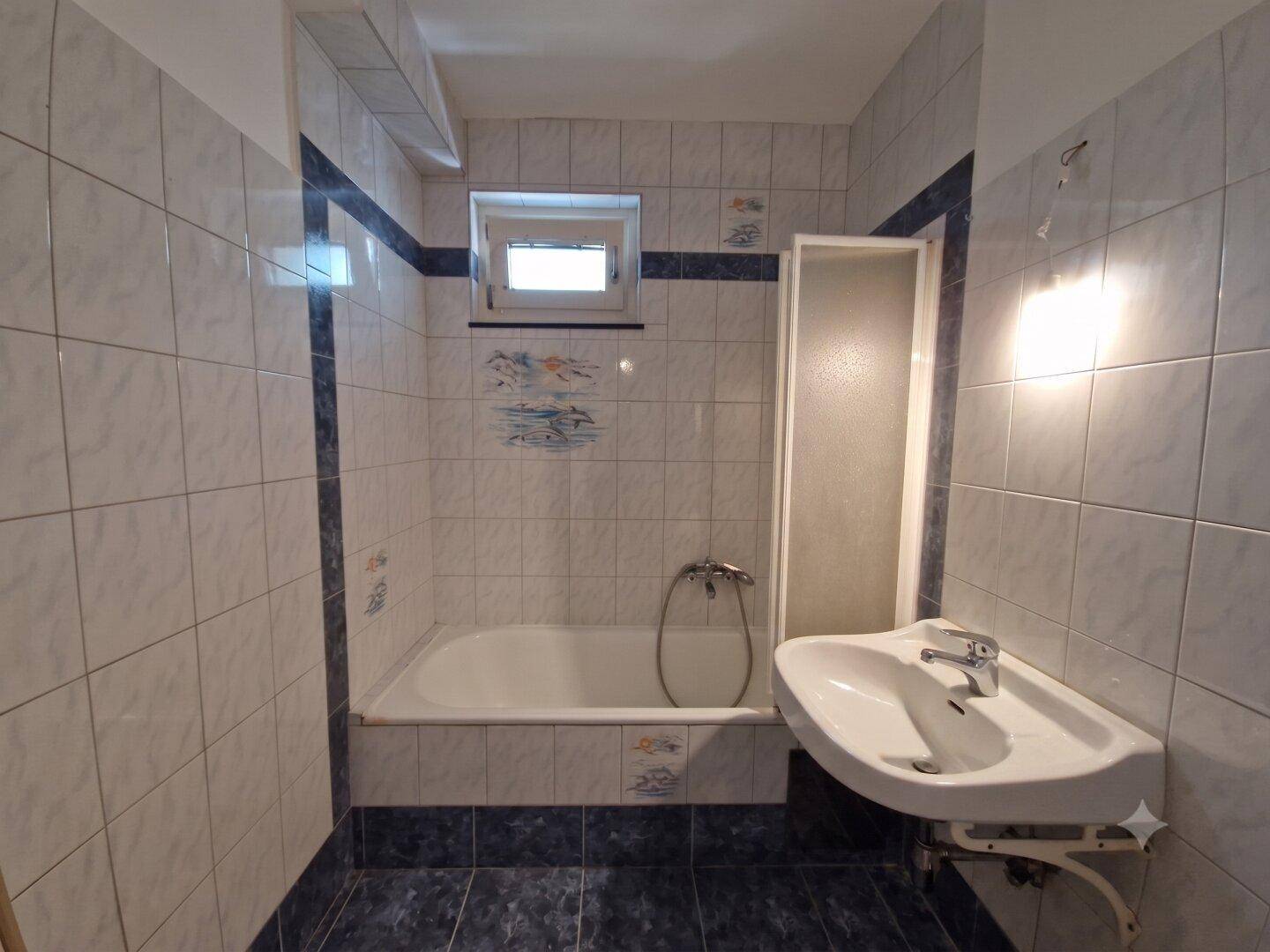 Badezimmer mit Badewanne, Waschbecken und blau-weißen Fliesen, inklusive kleinem Fenster.