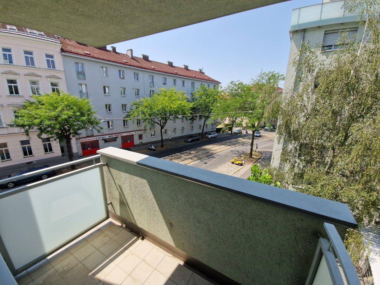 Blick vom Balkon auf eine belebte Straße mit Bäumen und umliegenden Gebäuden.