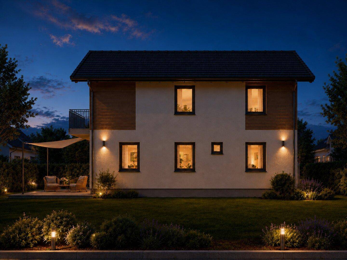 Rückseite des modernen Hauses bei Nacht mit beleuchteter Terrasse und weitläufigem Garten.
