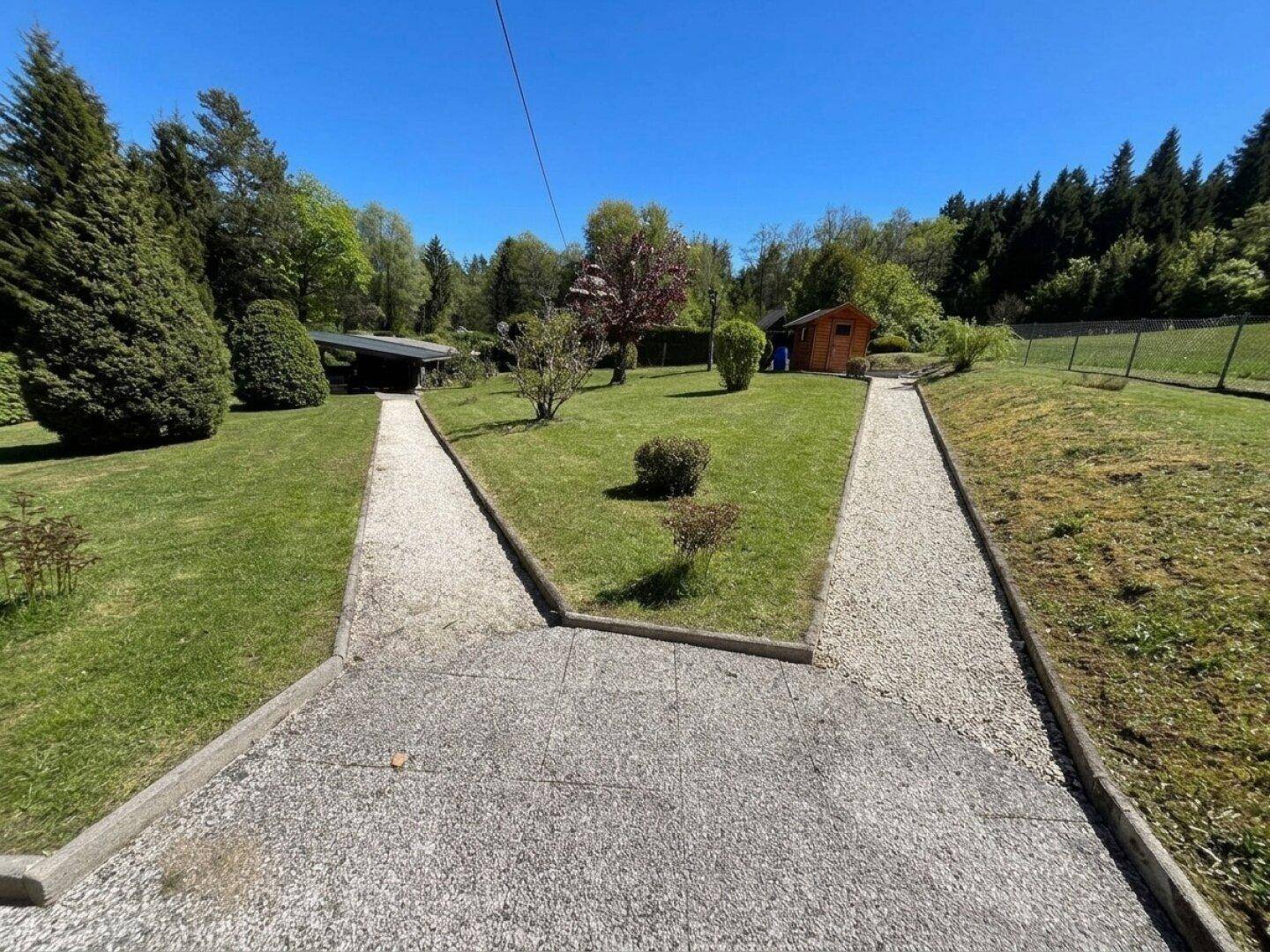 Gepflegter Garten mit Kieswegen, Rasenflächen und einem kleinen Holzschuppen im Hintergrund.