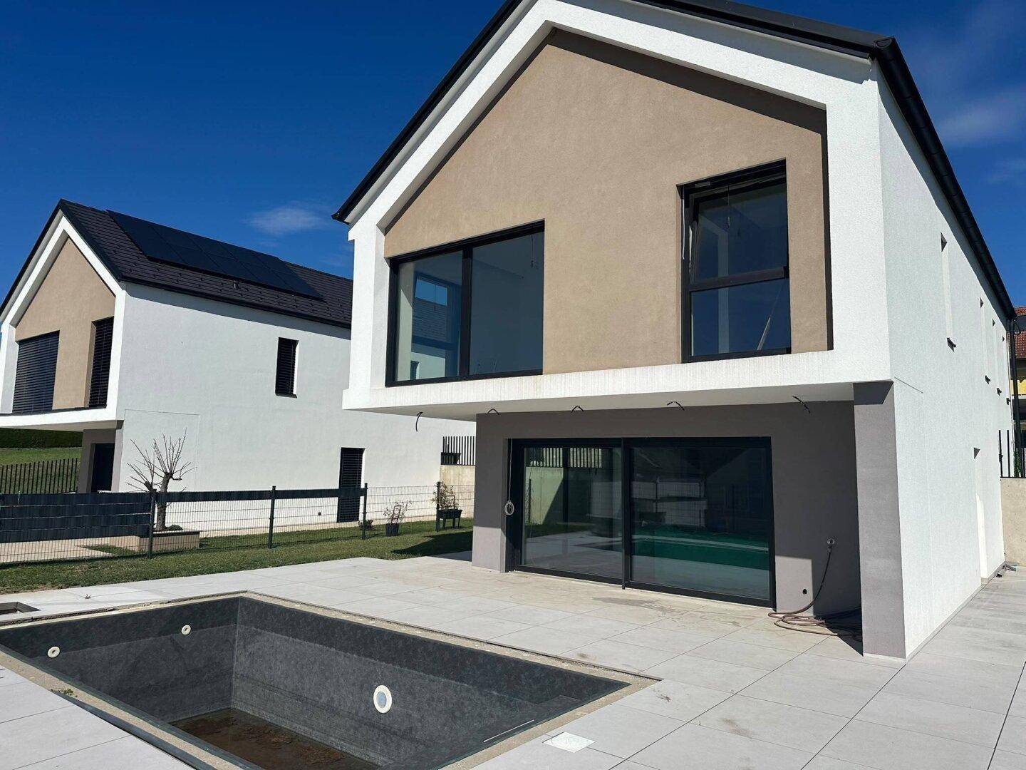 Modernes Haus mit heller Fassade, großen Fenstern und einem leeren Pool im Außenbereich.