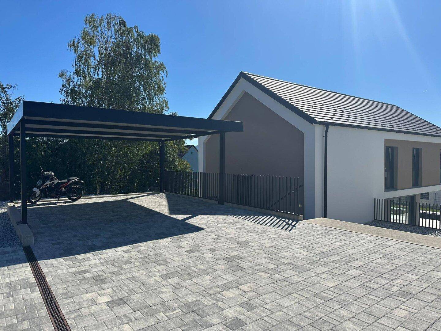Überdachter Carport und gepflasterte Einfahrt neben dem modernen Einfamilienhaus.