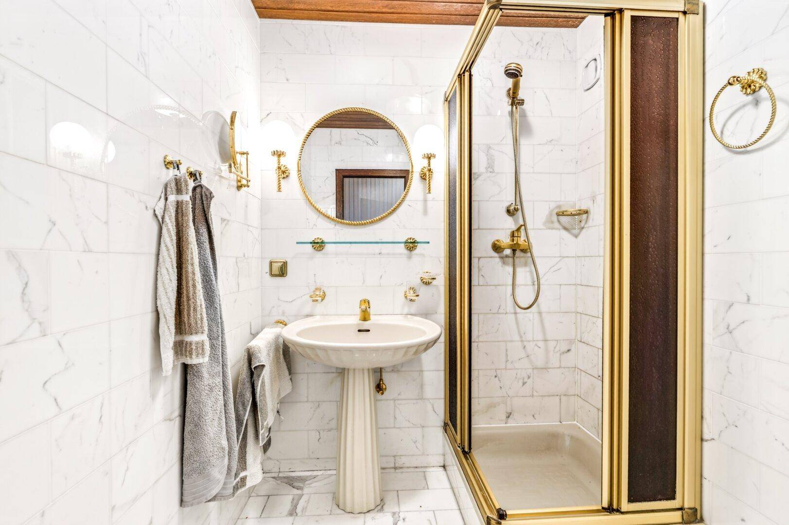 Elegantes Badezimmer mit Marmorfliesen, goldfarbenen Armaturen und einer Duschkabine.