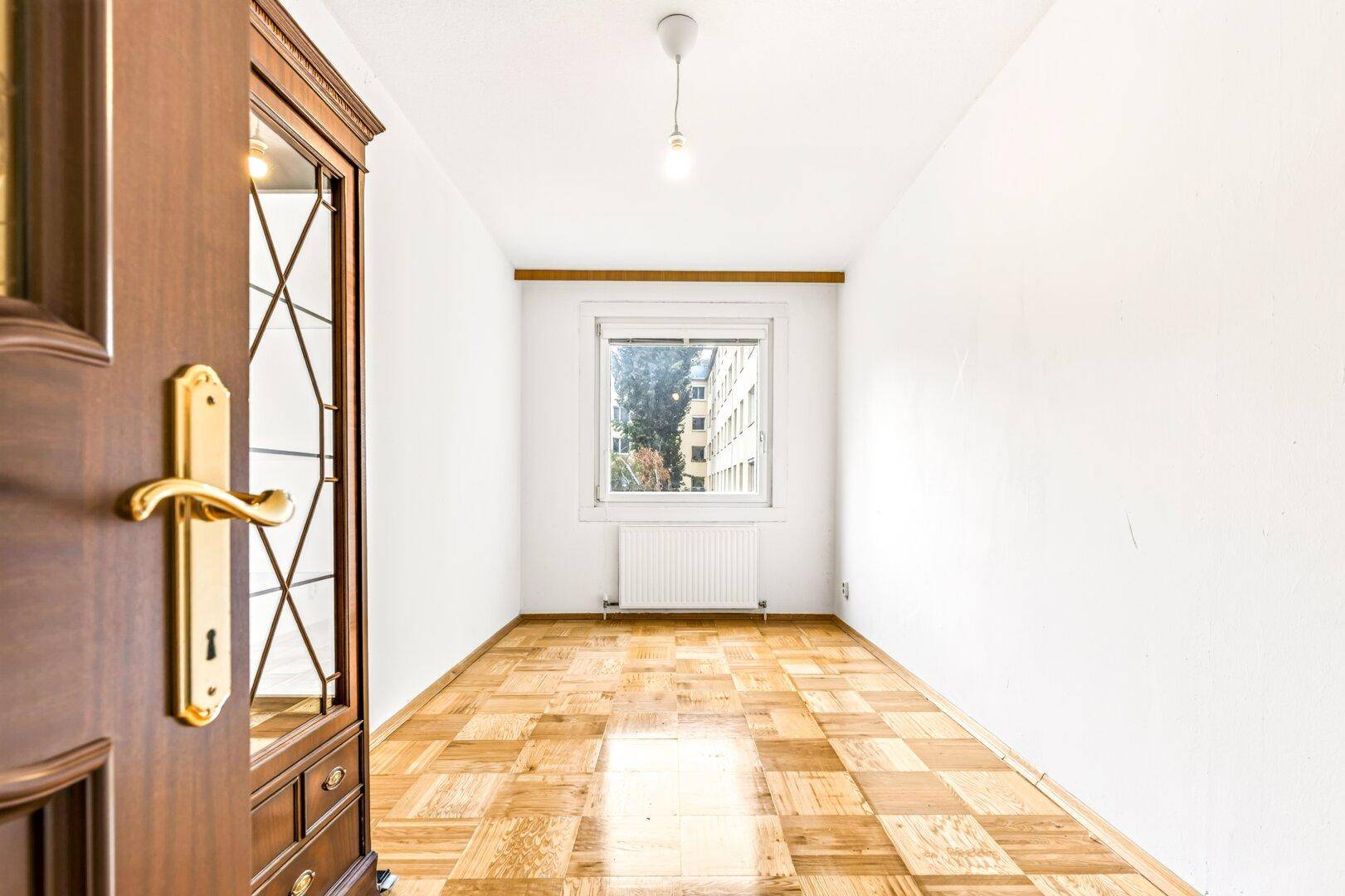 Helles, leeres Zimmer mit Parkettboden und weißen Wänden, bereit zur individuellen Gestaltung.