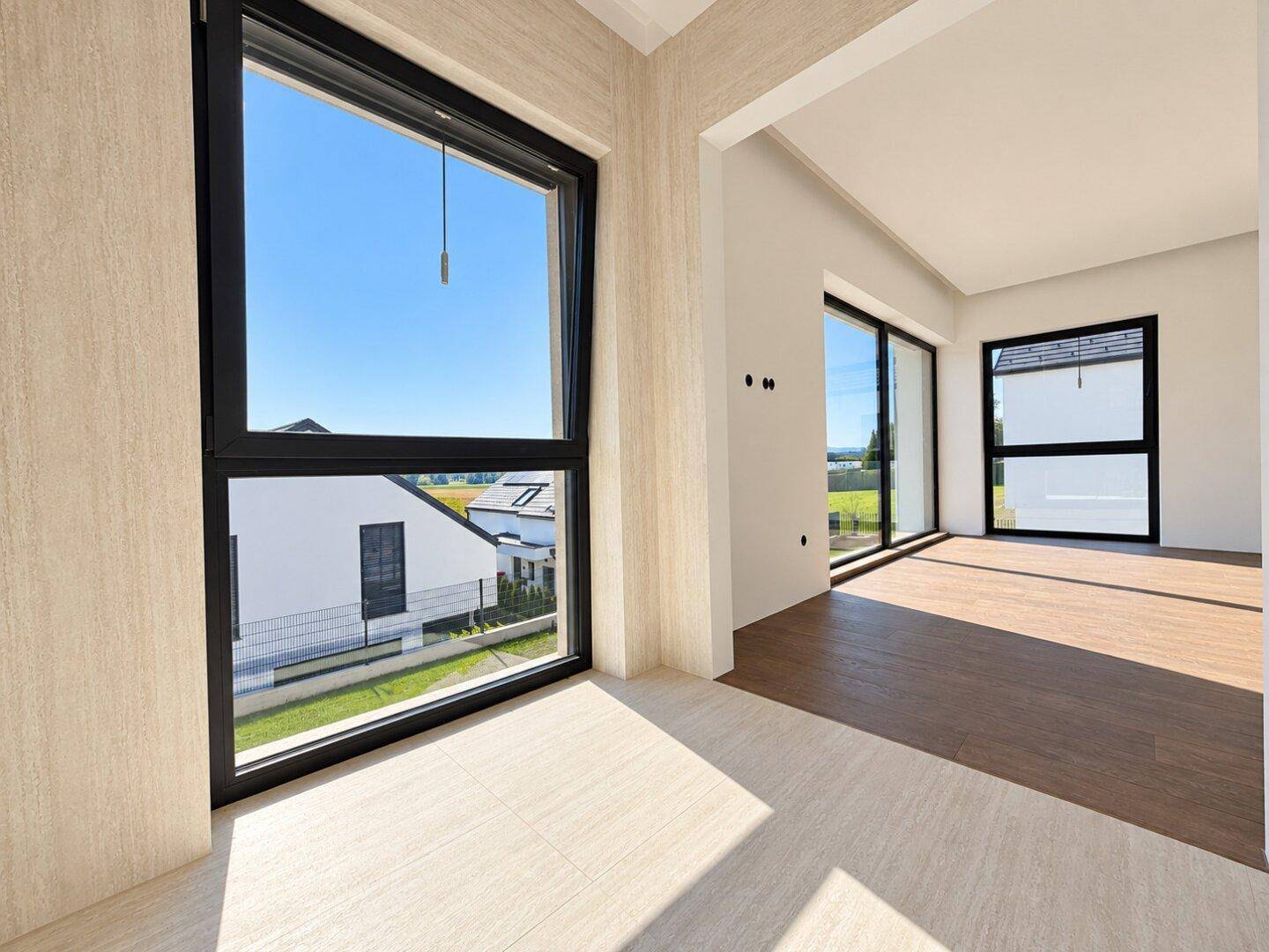 Heller, leerer Wohnraum mit großen Fenstern und Blick auf die Umgebung.