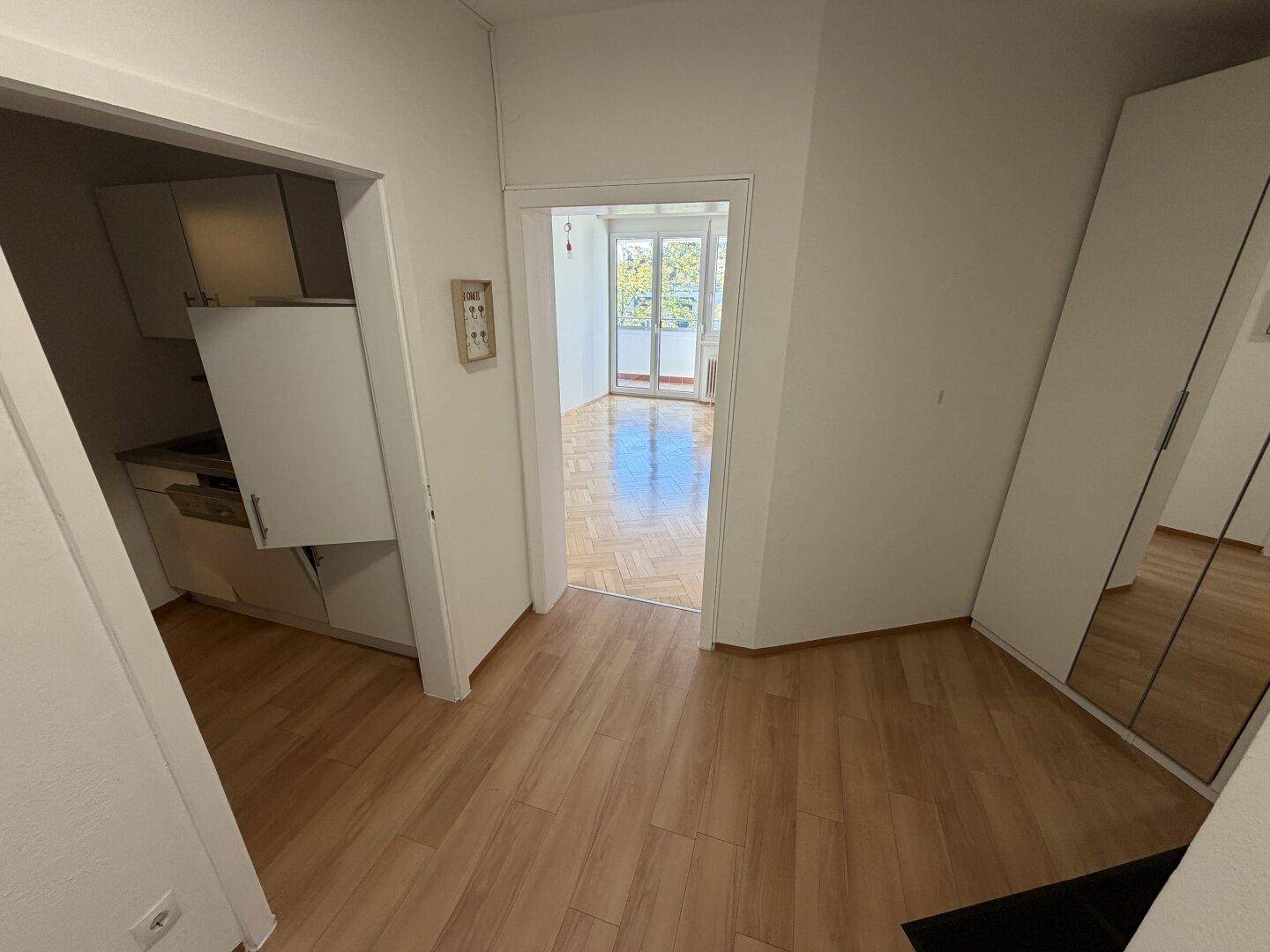 Flur mit Laminatboden, der zu einer kleinen Küche und einem weiteren Zimmer führt.