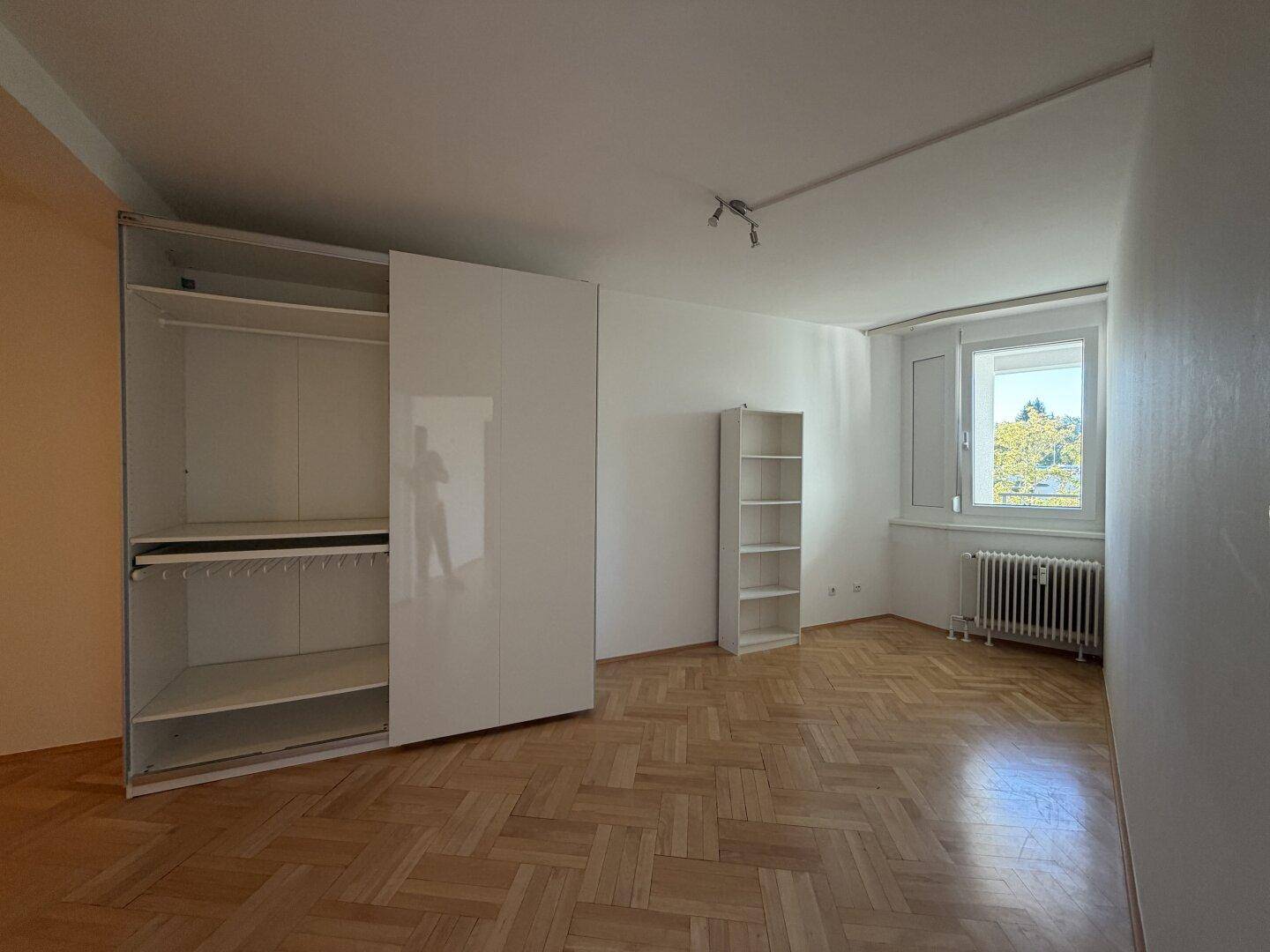 Schlafzimmer mit Parkettboden, großem Einbauschrank und Fenster mit Blick ins Grüne.