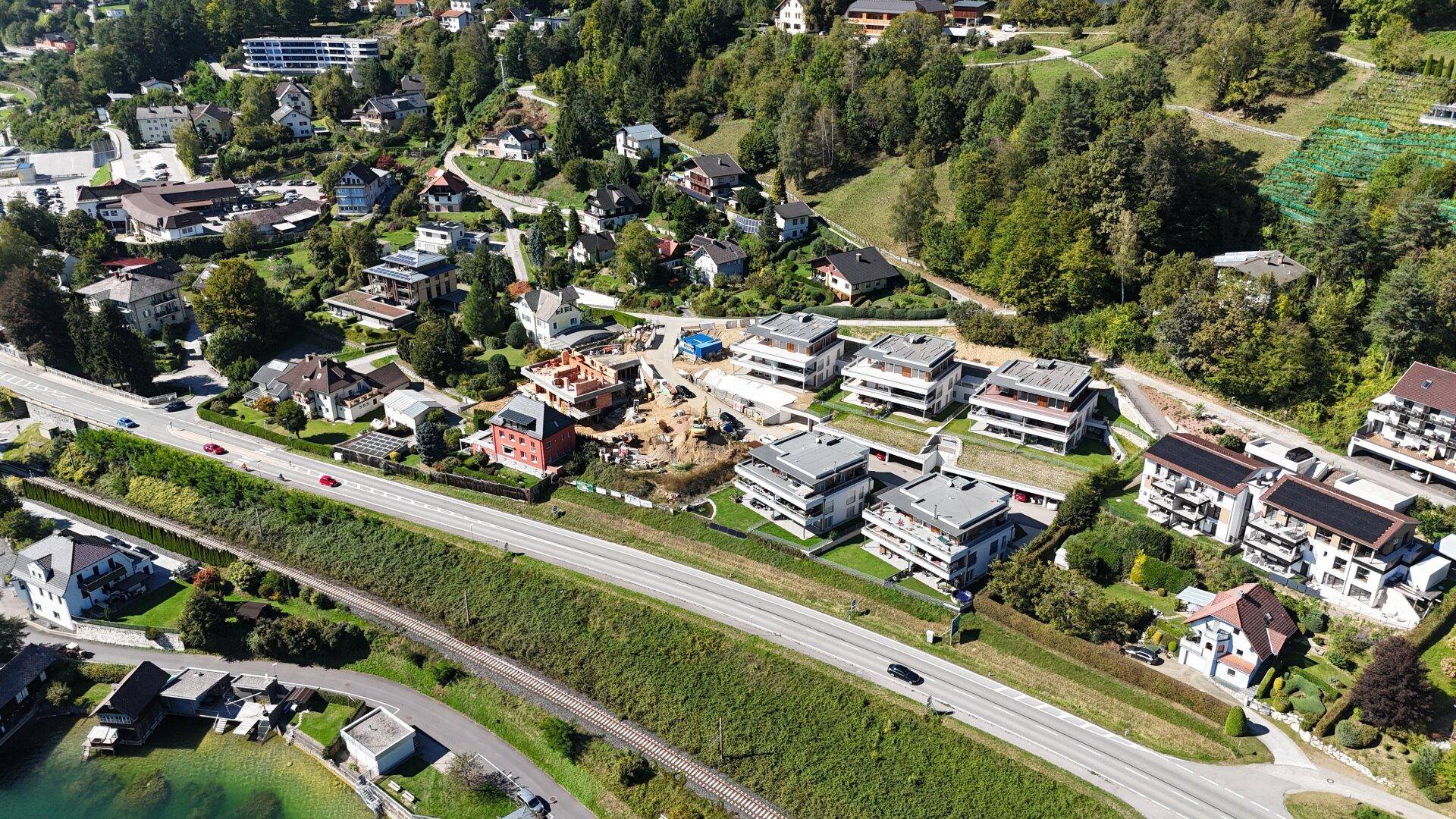 Weitläufige Luftaufnahme einer Baustelle am Seeufer mit neuen Wohnkomplexen und Straße.