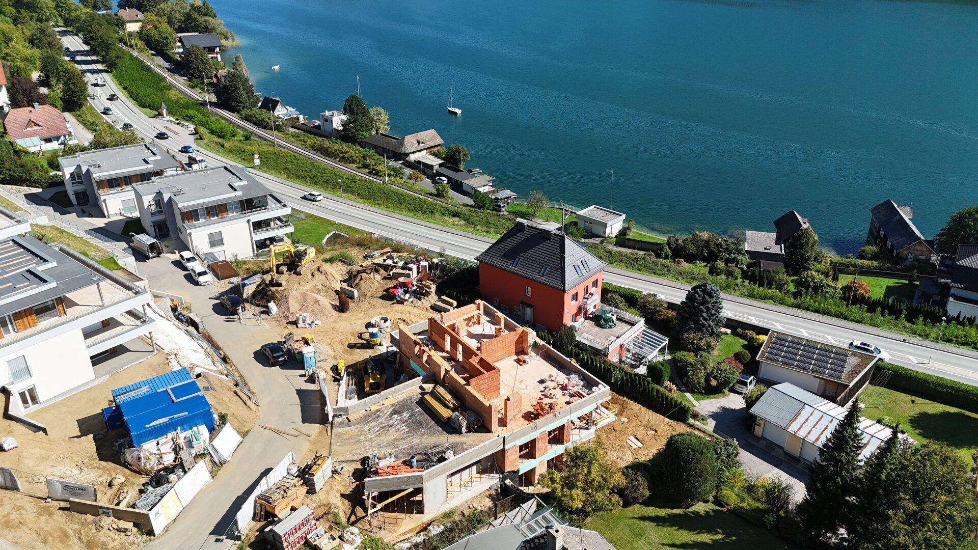 Detailansicht einer Baustelle mit Rohbau und Blick auf den See sowie die Uferstraße.
