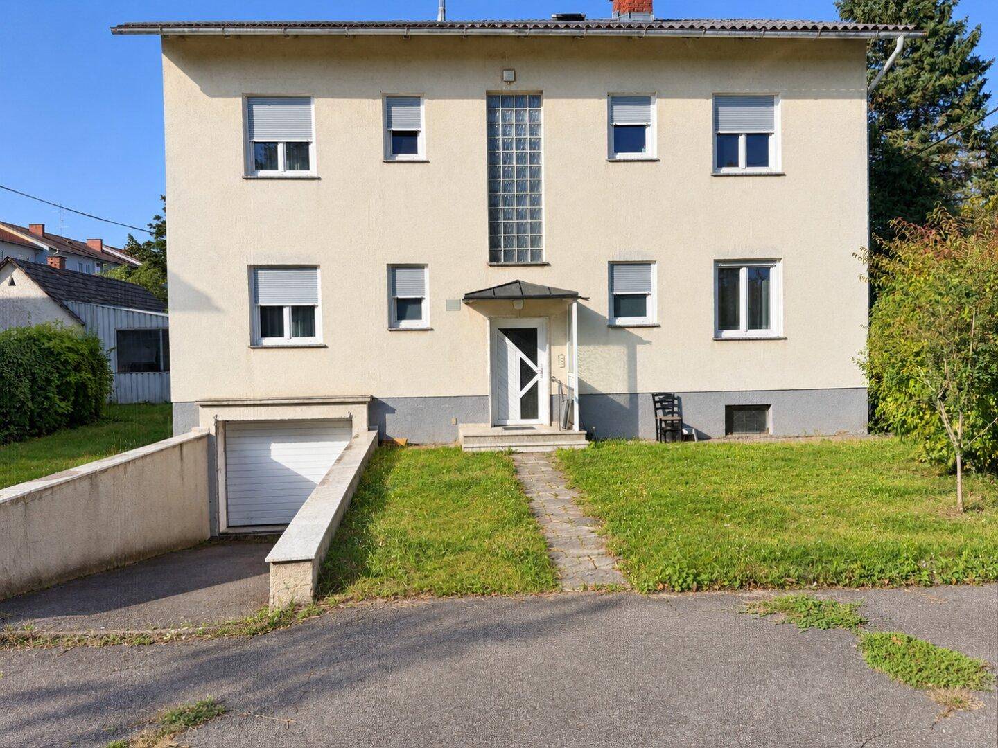 Vorderansicht des Hauses mit Garagenzufahrt, Eingangsbereich und Rollläden an den Fenstern, gut gepflegt.