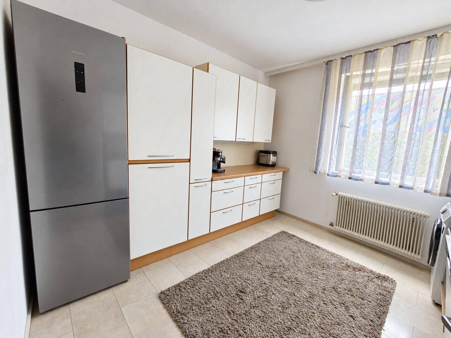 Funktionale Küche mit weißen Schränken, großem Kühlschrank und Fenster.