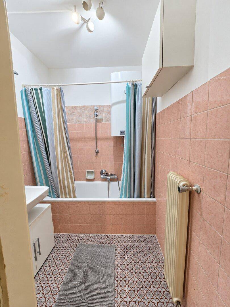 Badezimmer mit Badewanne, rosa Fliesen und Heizkörper.