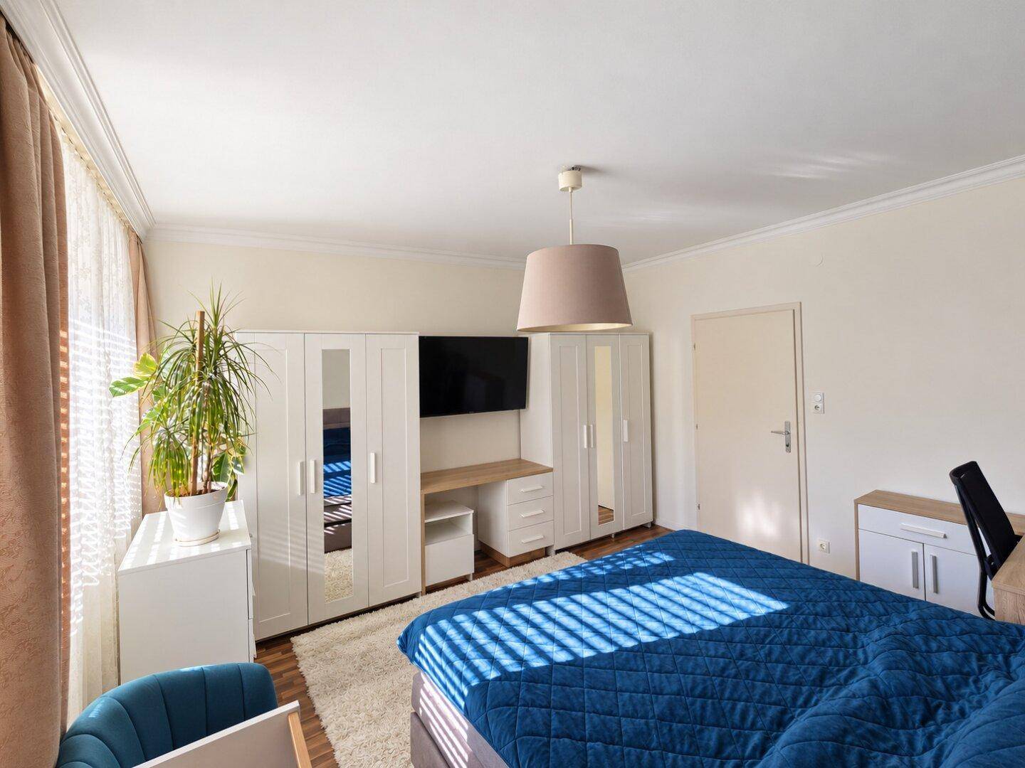 Gemütliches Schlafzimmer mit Doppelbett, Kleiderschränken und viel Tageslicht.
