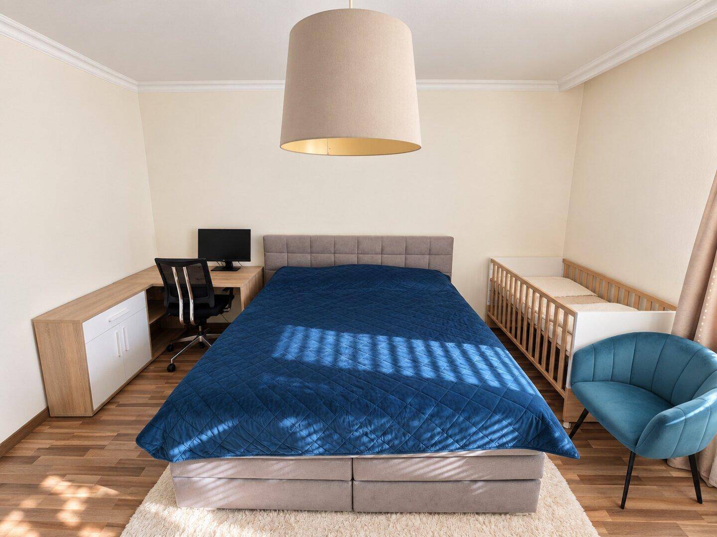 Helles Schlafzimmer mit großem Bett, Schreibtisch und Babybett.