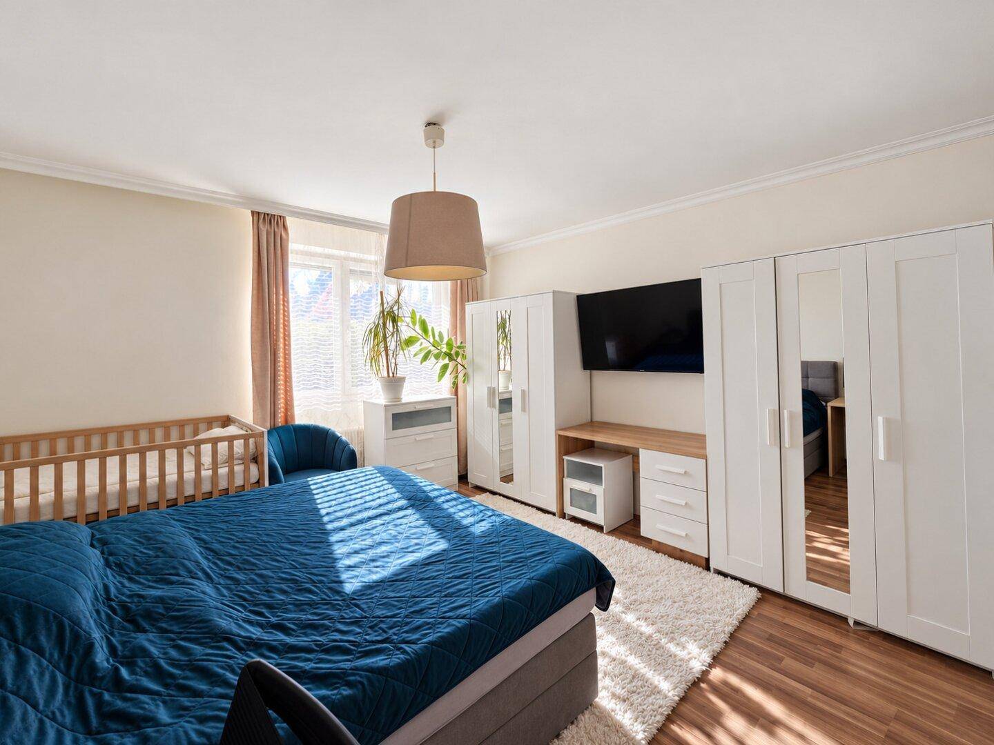 Geräumiges Schlafzimmer mit Doppelbett, Babybett und weißem Kleiderschrank.