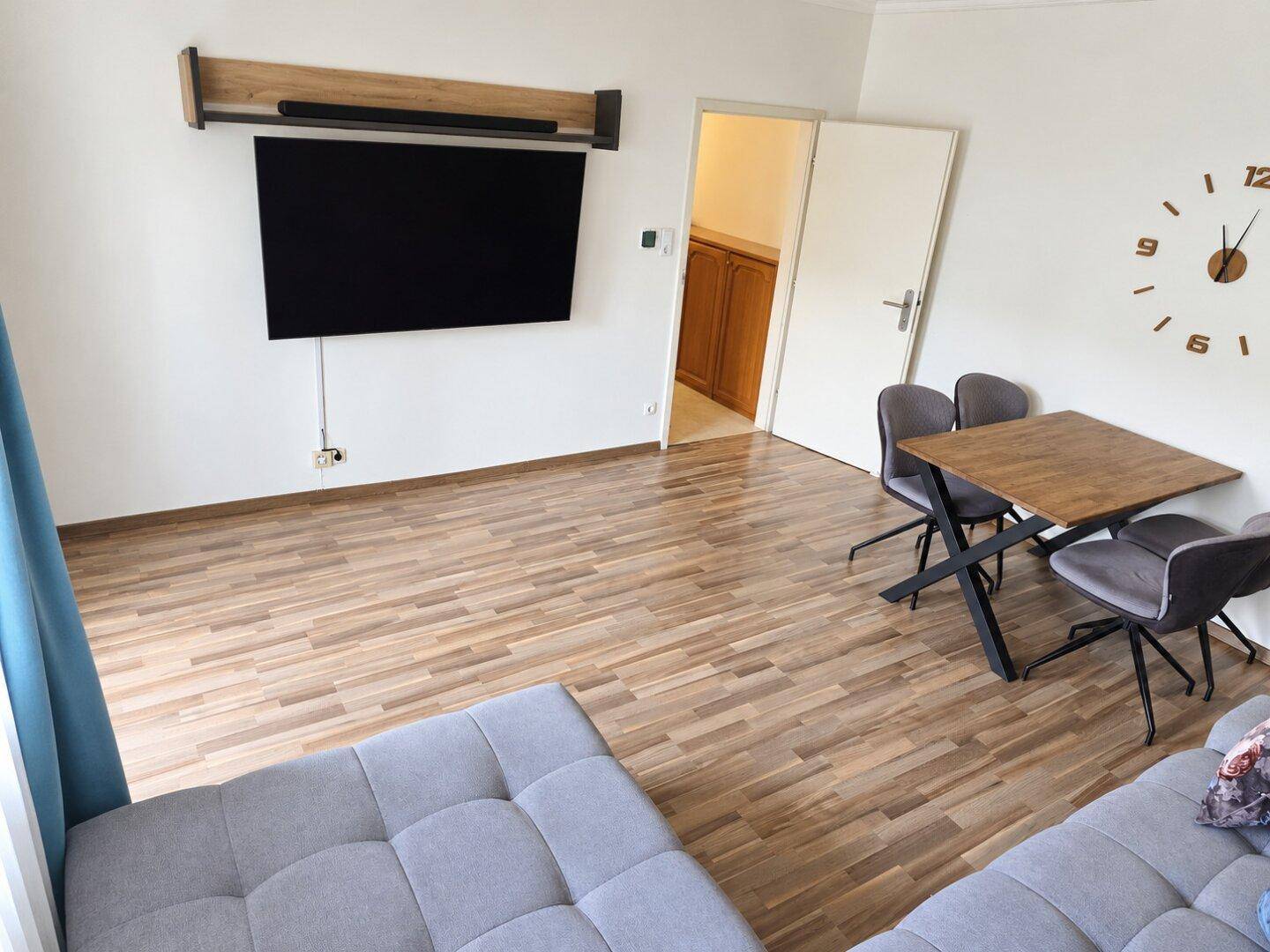 Geräumiger Wohnbereich mit Laminatboden, Wandfernseher und Essbereich.