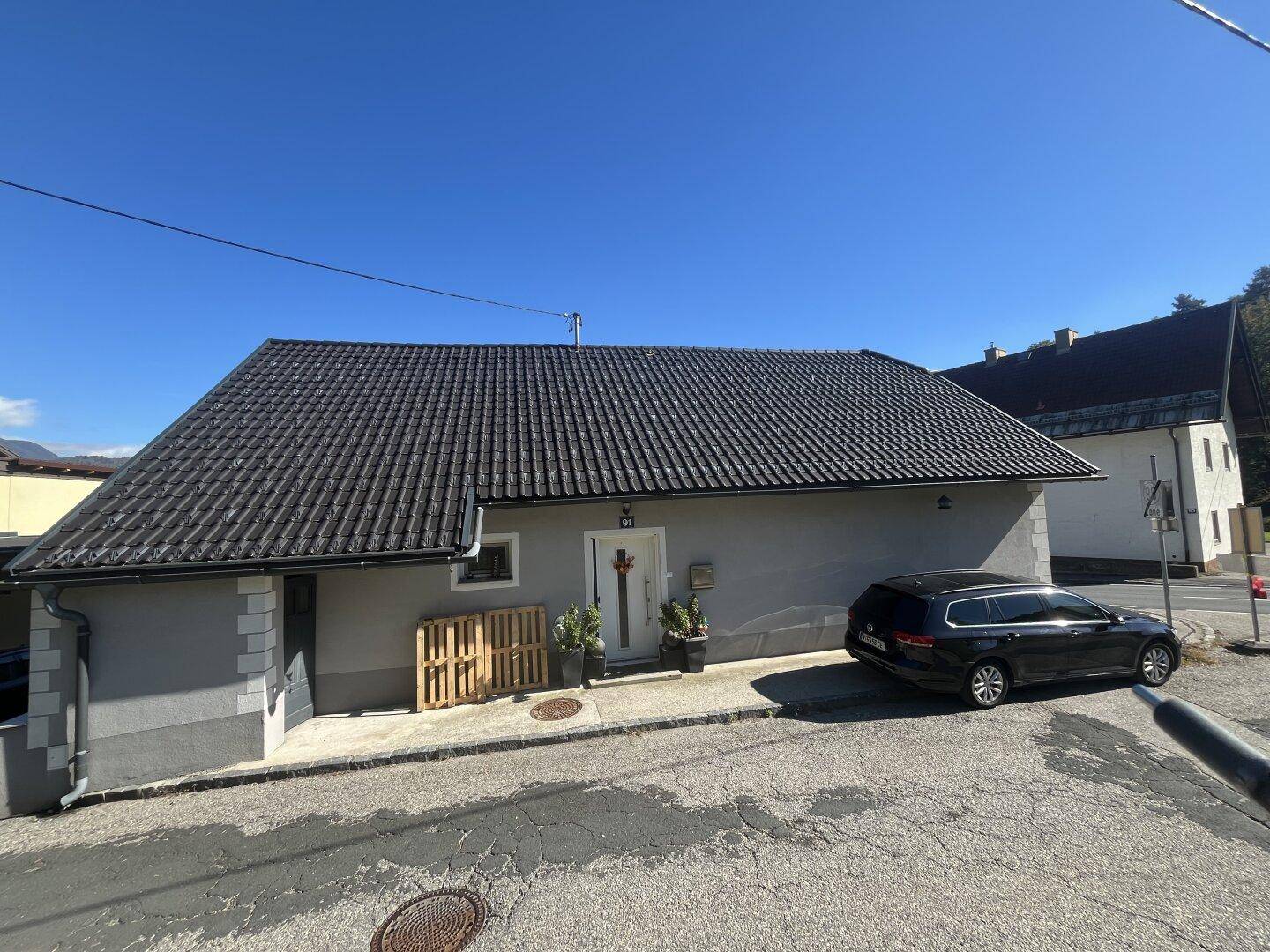 Vorderansicht des Einfamilienhauses mit grauer Fassade und dunklem Ziegeldach.
