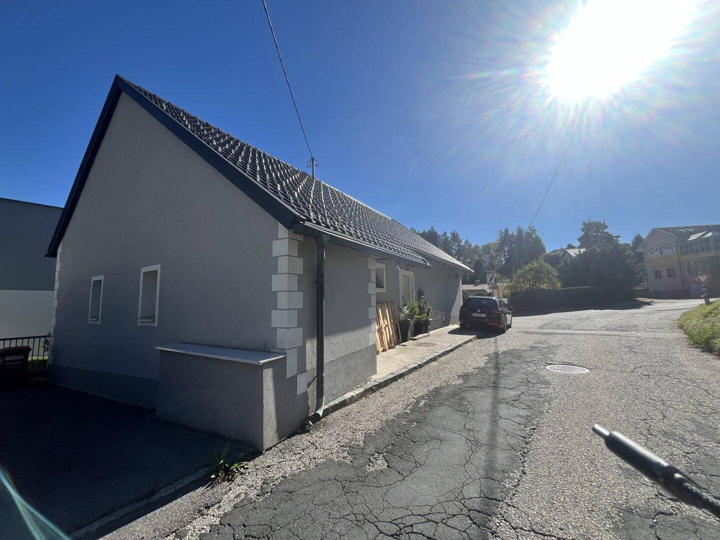 Seitenansicht des Hauses mit grauer Fassade, dunklem Dach und sonniger Ausrichtung.