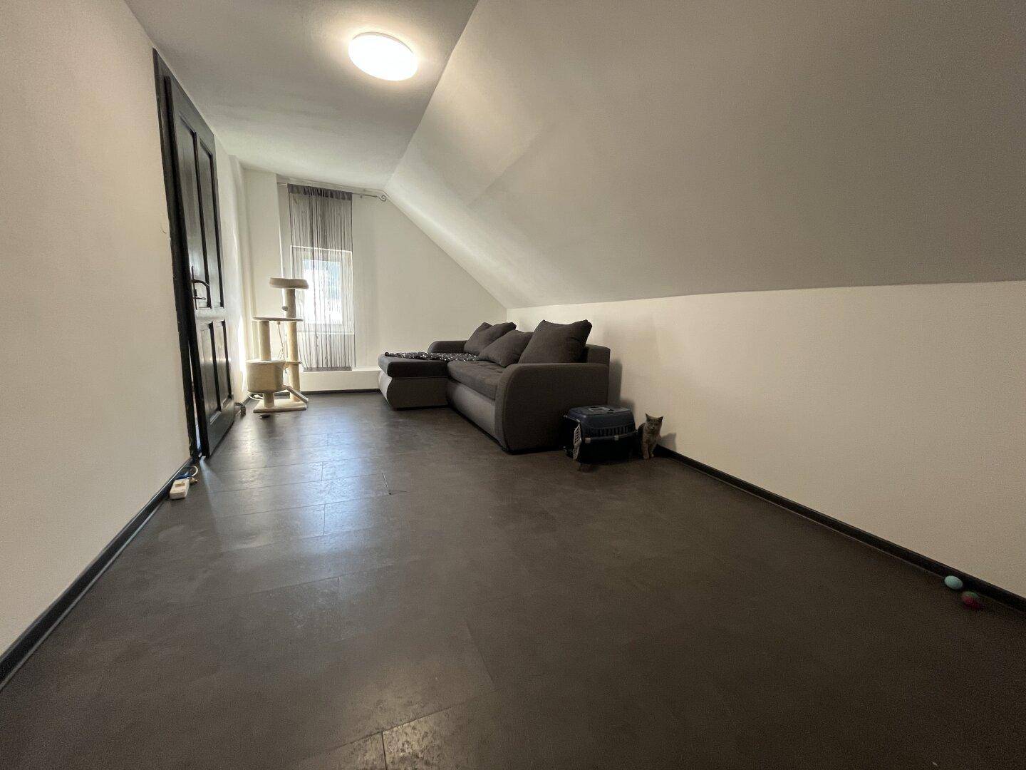Gemütlicher Wohnbereich im Dachgeschoss mit Sofa, dunklem Boden und schrägen Wänden.