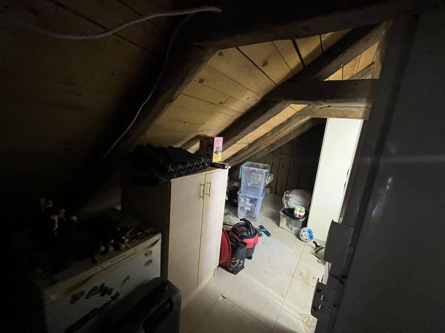 Unausgebauter Dachboden mit sichtbaren Holzbalken und Stauraum für diverse Gegenstände.