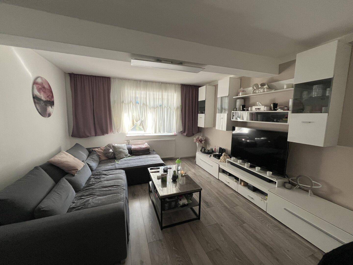 Modern eingerichtetes Wohnzimmer mit großem Sofa, TV-Möbeln und Laminatboden.