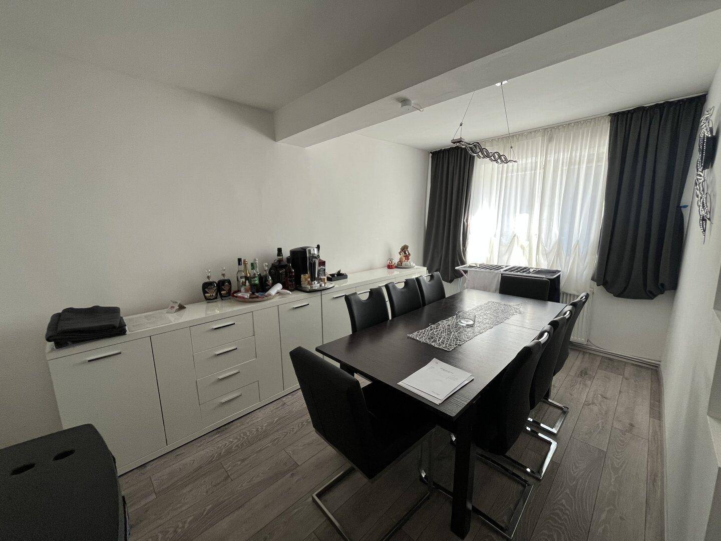 Heller Essbereich mit großem Esstisch, Sideboard und Laminatboden.