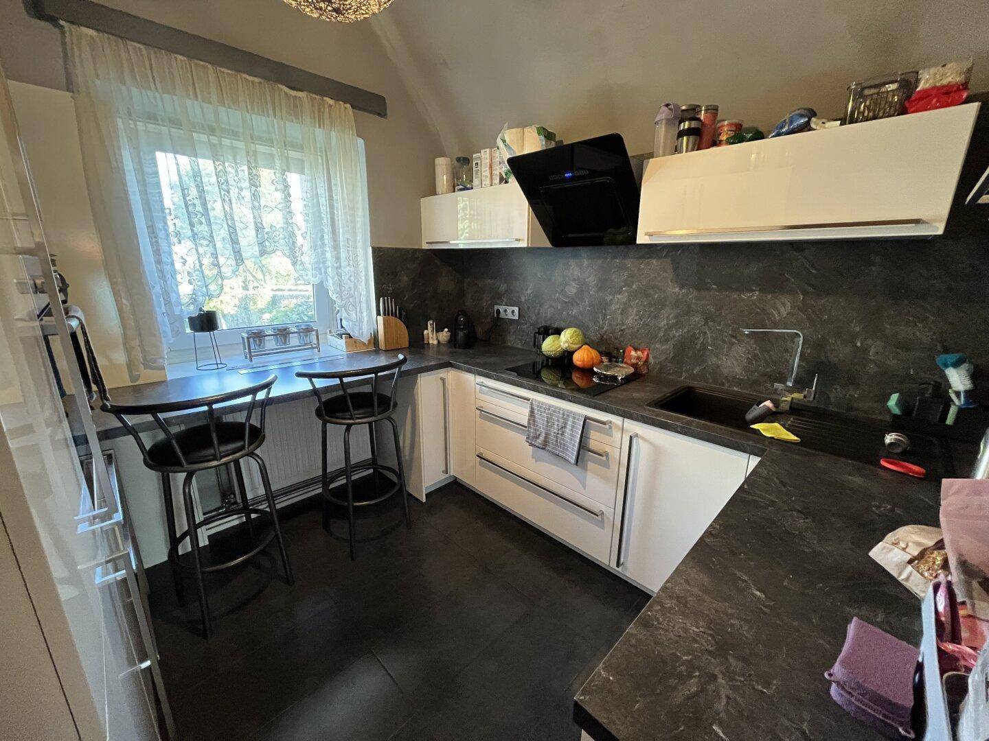 Moderne Küche mit weißen Schränken, dunkler Arbeitsplatte und integrierter Frühstücksbar.