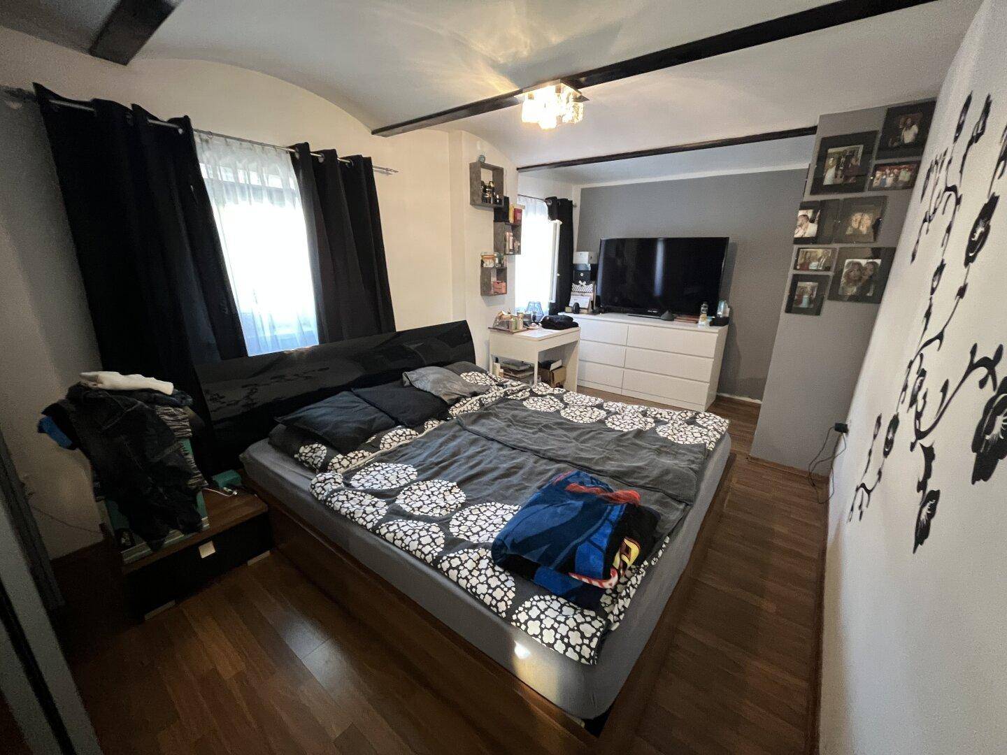Gemütliches Schlafzimmer mit Doppelbett, Holzbalken und dunklen Vorhängen.