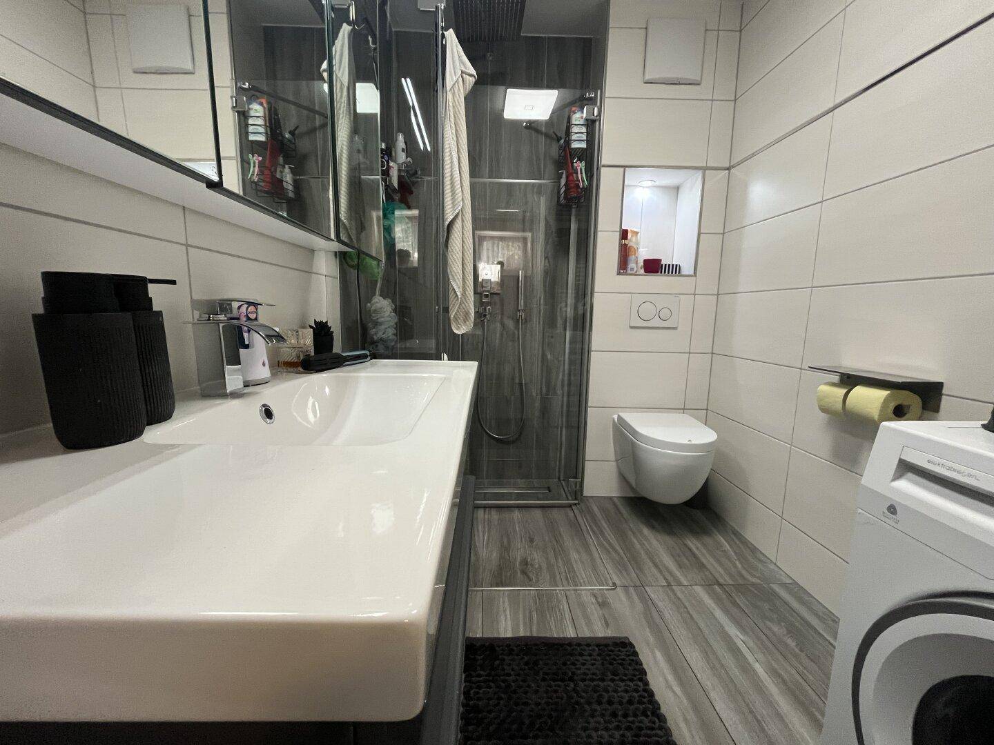 Modernes Badezimmer mit großer begehbarer Dusche, Waschbecken und Wand-WC.