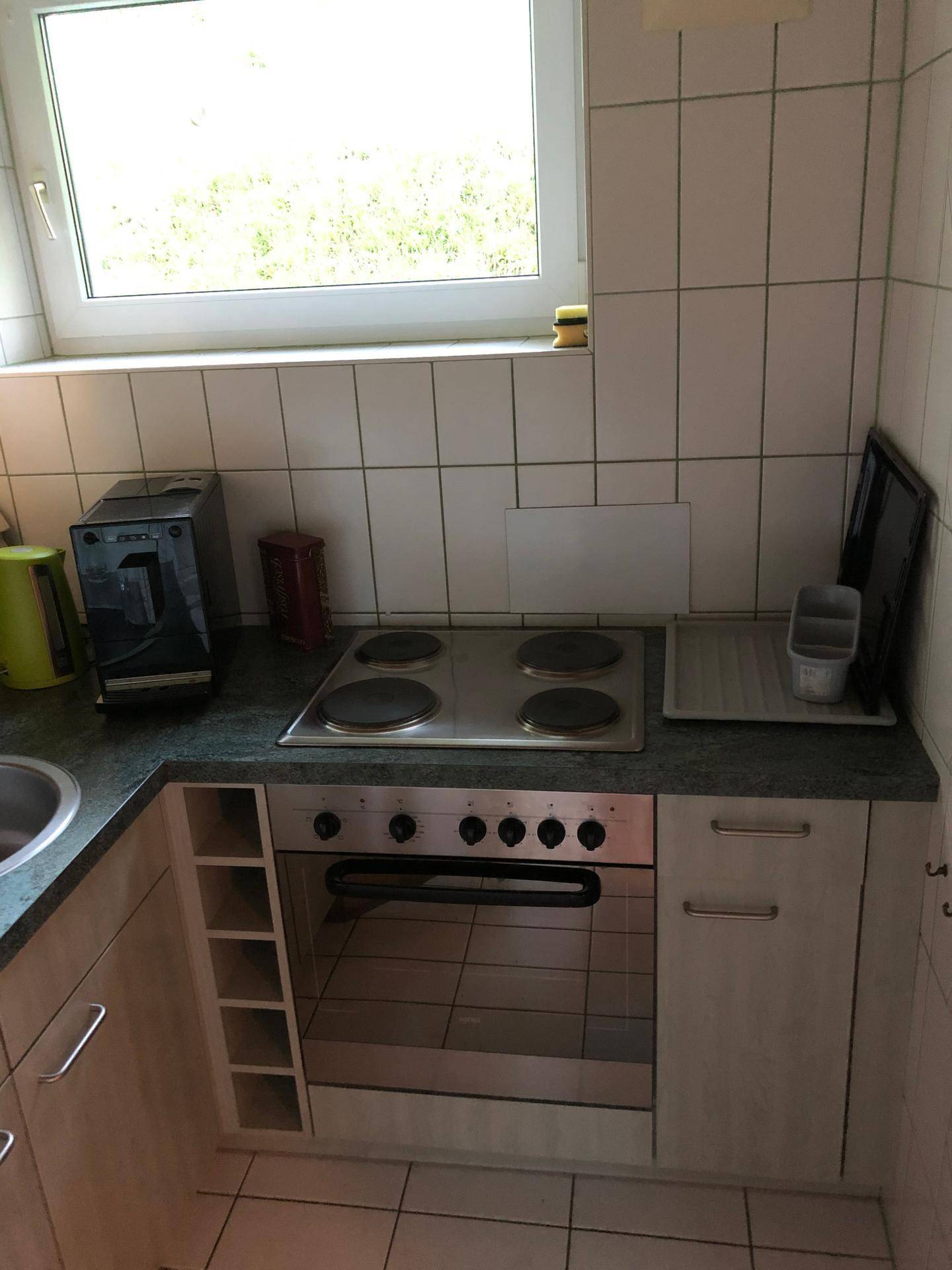 Küche mit weißen Fliesen, Fenster, Elektroherd mit Backofen und Spülbecken.