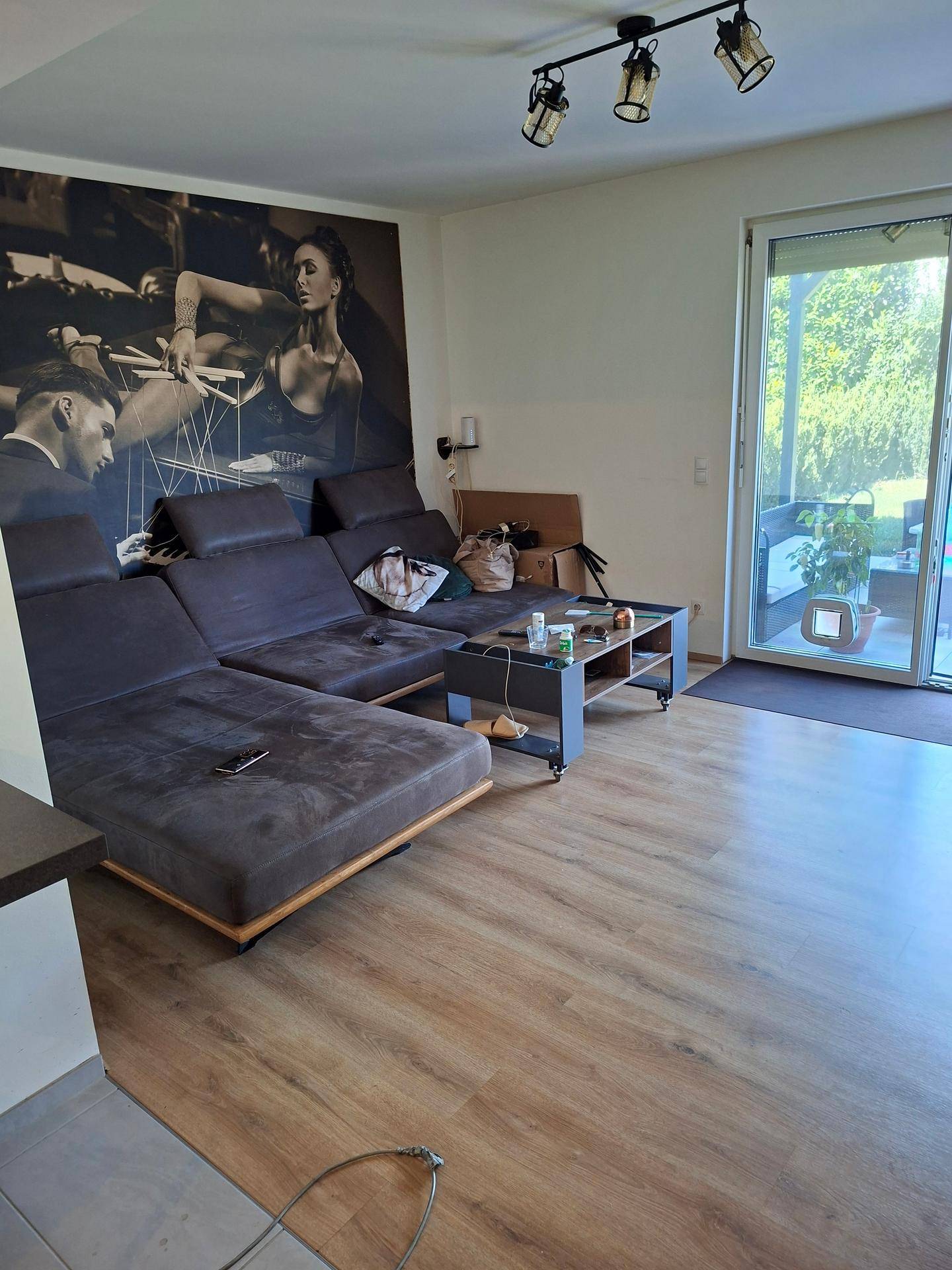 Geräumiges Wohnzimmer mit großer Eckcouch, Wandbild und Zugang zur Terrasse.