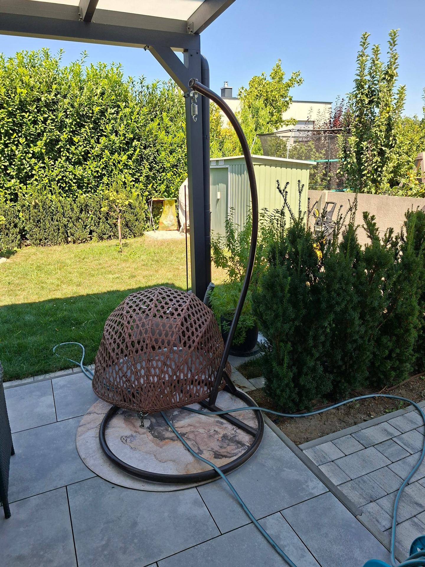 Terrasse mit Hängesessel und Blick auf den gepflegten Garten mit Schuppen im Hintergrund.