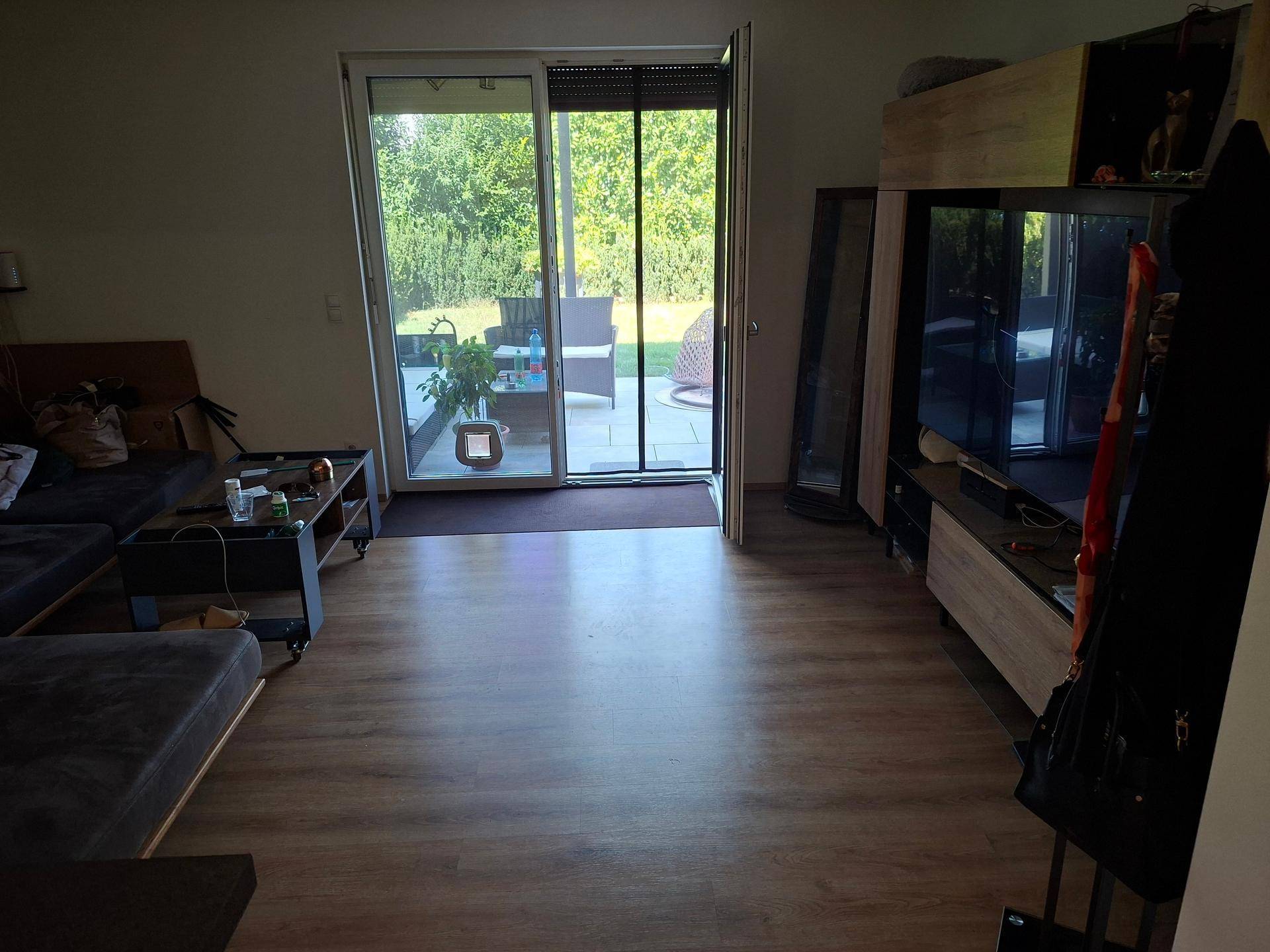 Wohnzimmer mit Laminatboden, TV-Möbel und großzügigem Blick auf die Terrasse und den Garten.