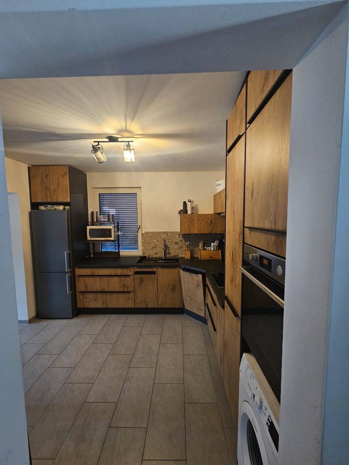 Geräumige Küche mit L-förmiger Anordnung, Holzfronten und Fliesenboden.