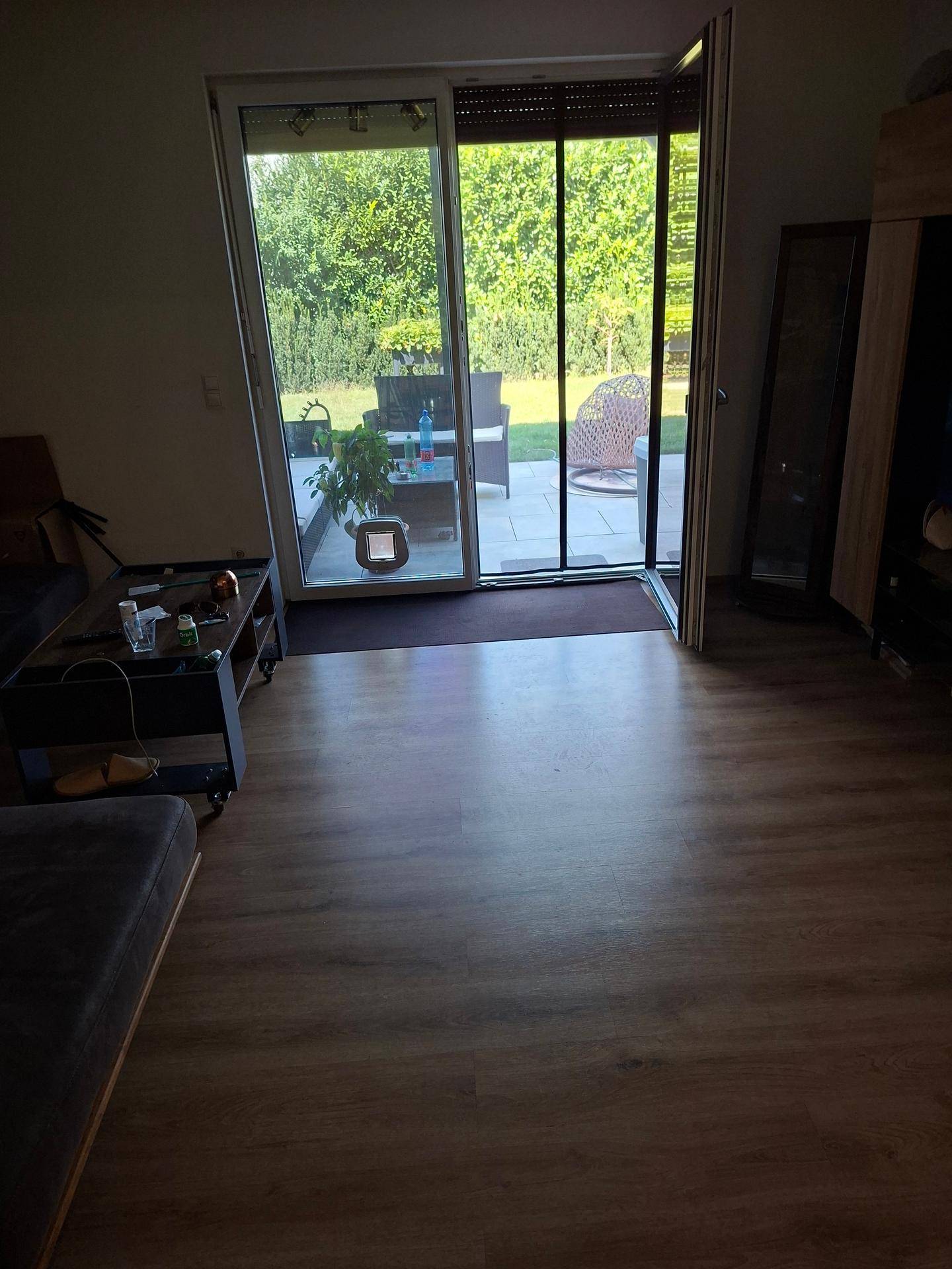 Wohnzimmer mit Laminatboden und großer Glasfront, die direkten Zugang zum Garten bietet.