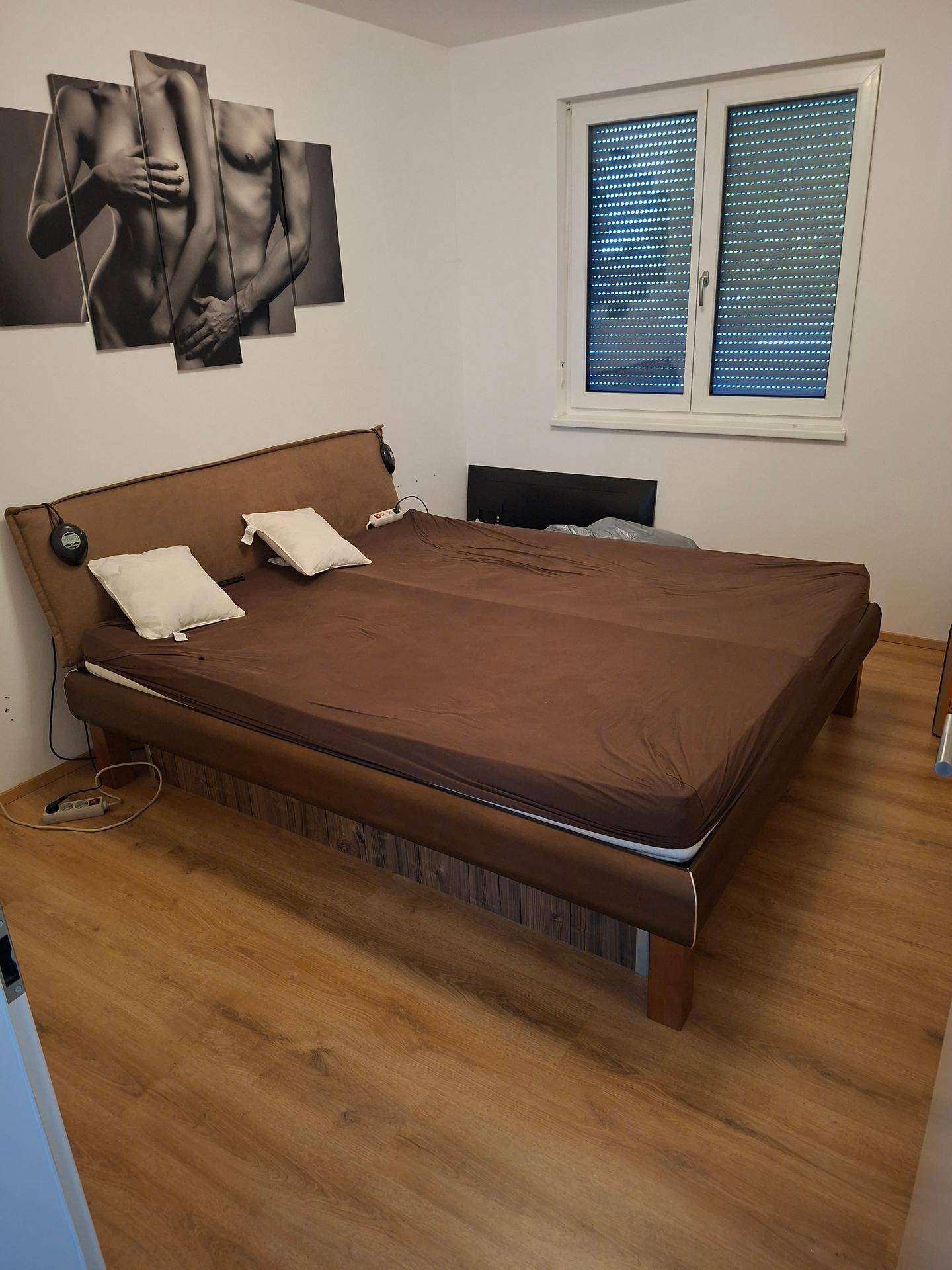 Schlafzimmer mit Doppelbett, Laminatboden und Fenster mit Rollläden.