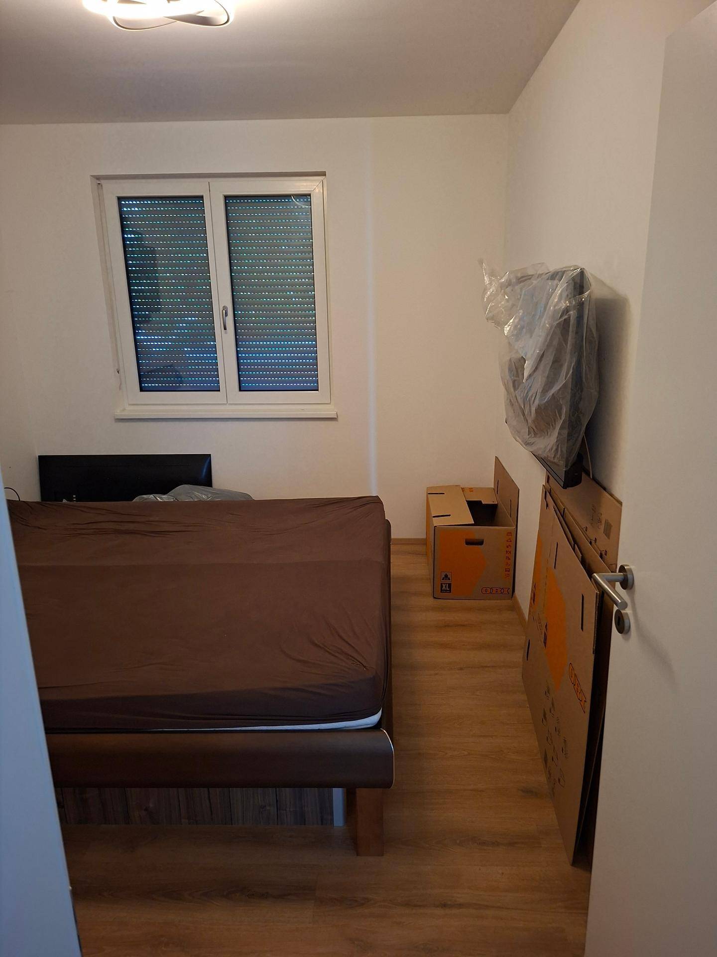 Schlafzimmer mit Laminatboden, Fenster und Kartons, die auf einen Umzug hindeuten.