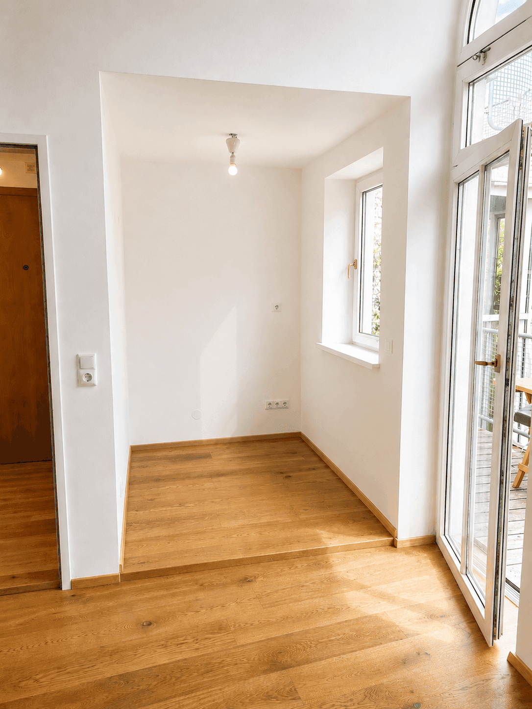 Leerer, heller Nischenbereich mit Fenster und Zugang zu einem Balkon.